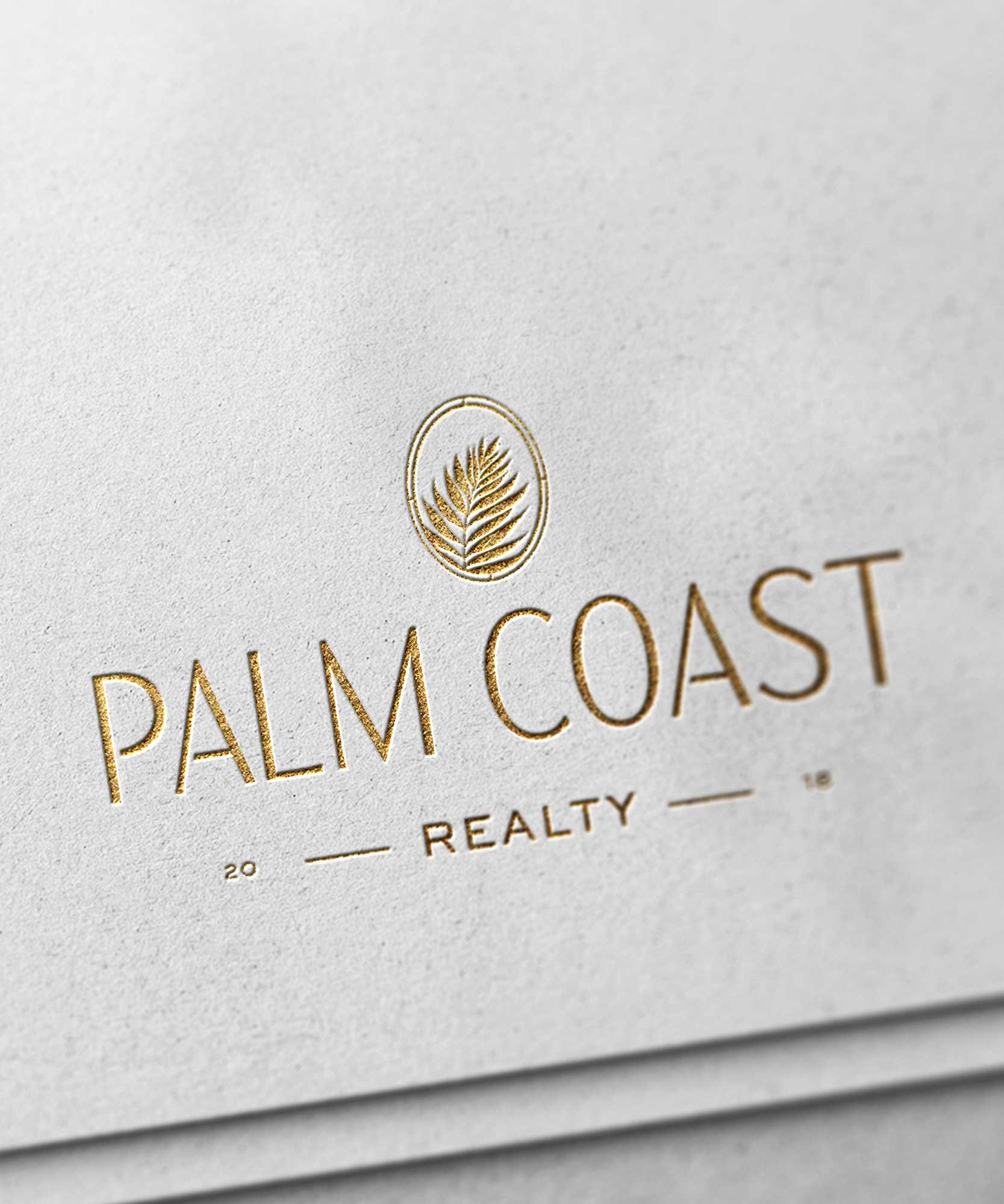 Close-up of a white paper with the Palm Coast Realty logo in gold foil, featuring a palm leaf inside a circular emblem.