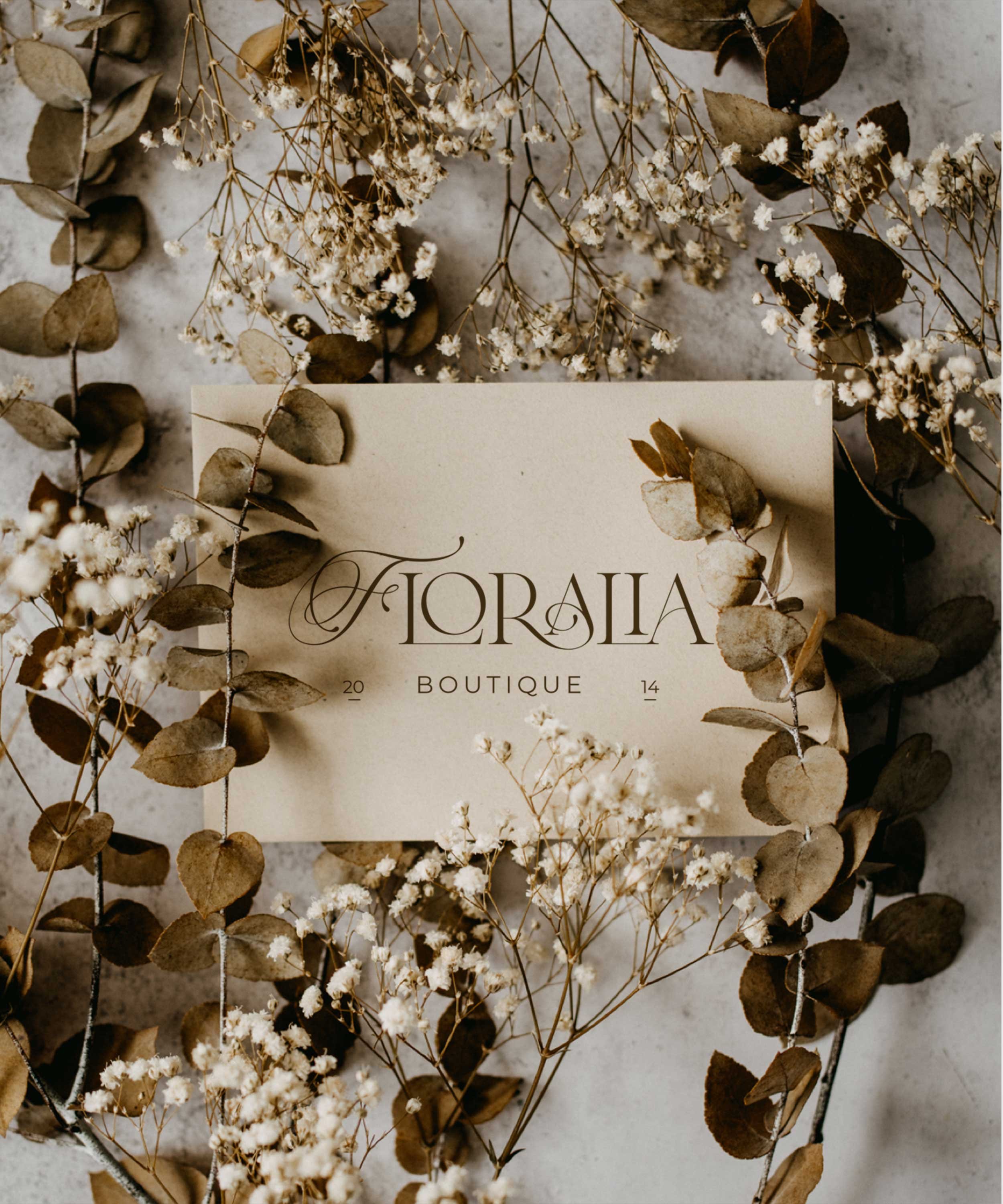 A beige card with the words "Floralia Boutique" surrounded by dried flowers and leaves on a light surface.