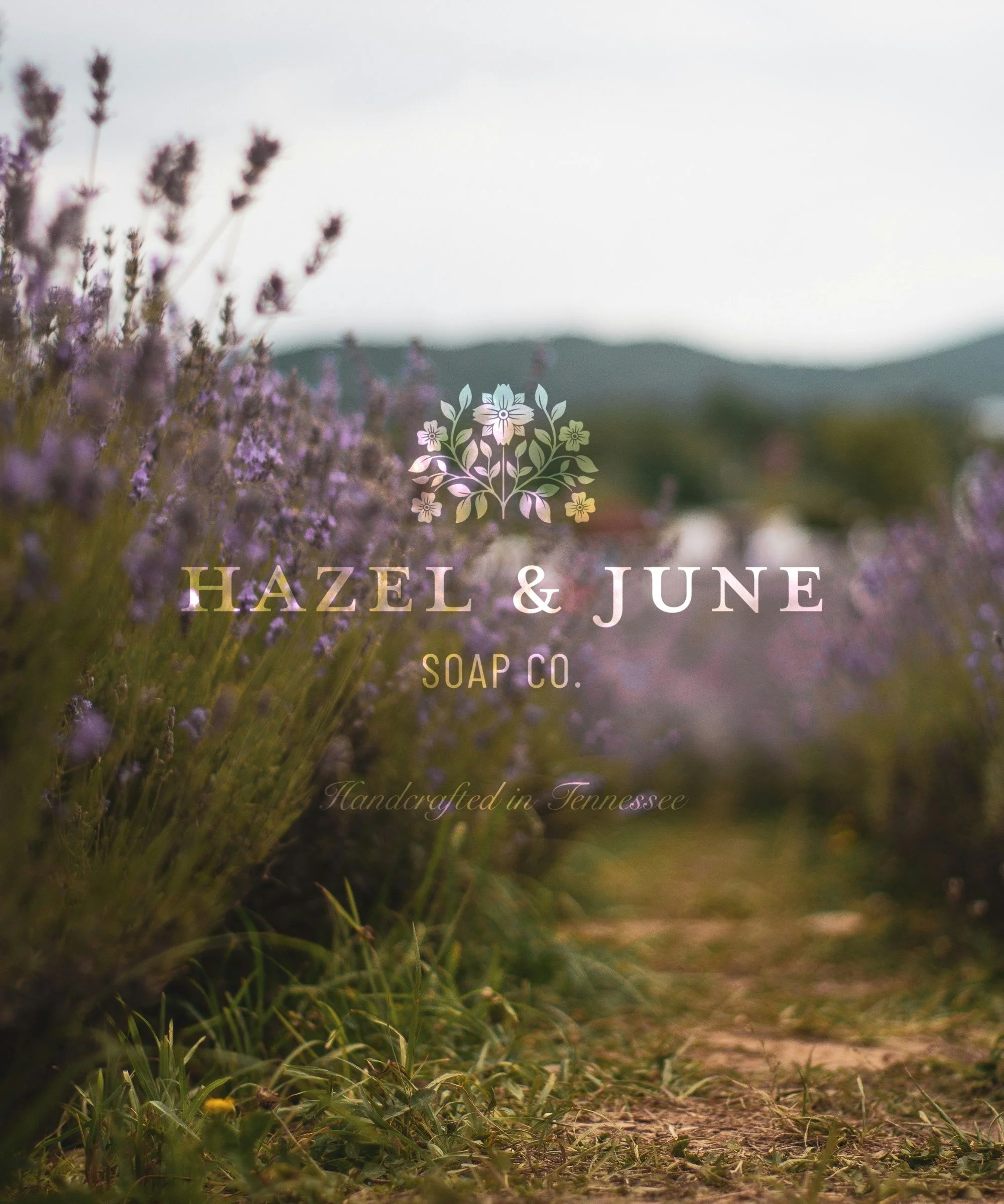 Brand logo for Hazel & June Soap Co. with a floral icon over a lavender field with mountains in the background, and the text 'Handcrafted in Tennessee'.