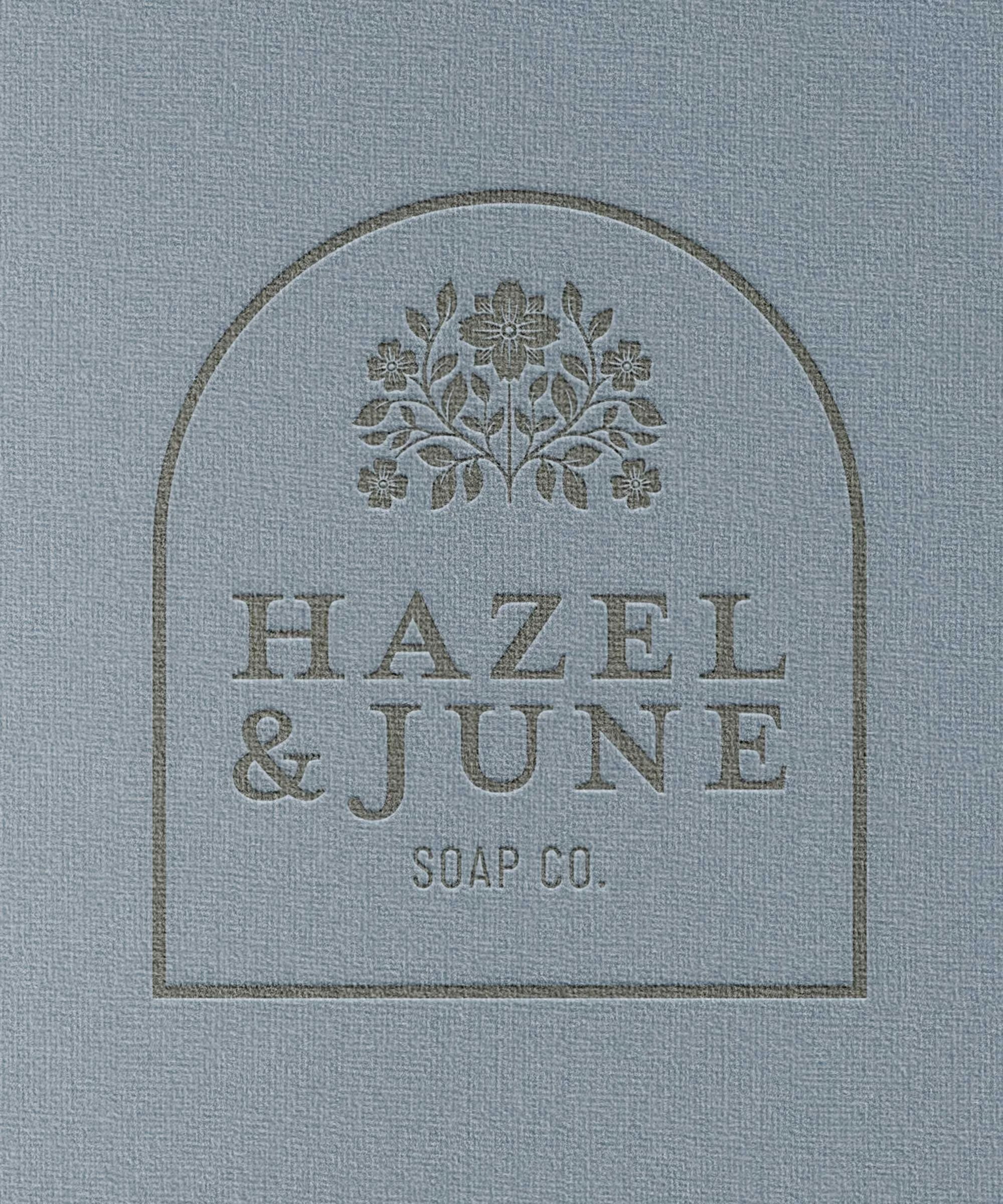 A soap packaging label with a floral design at the top, the text 'Hazel & June' in large font, and 'Soap Co.' below, all enclosed in an arched border.