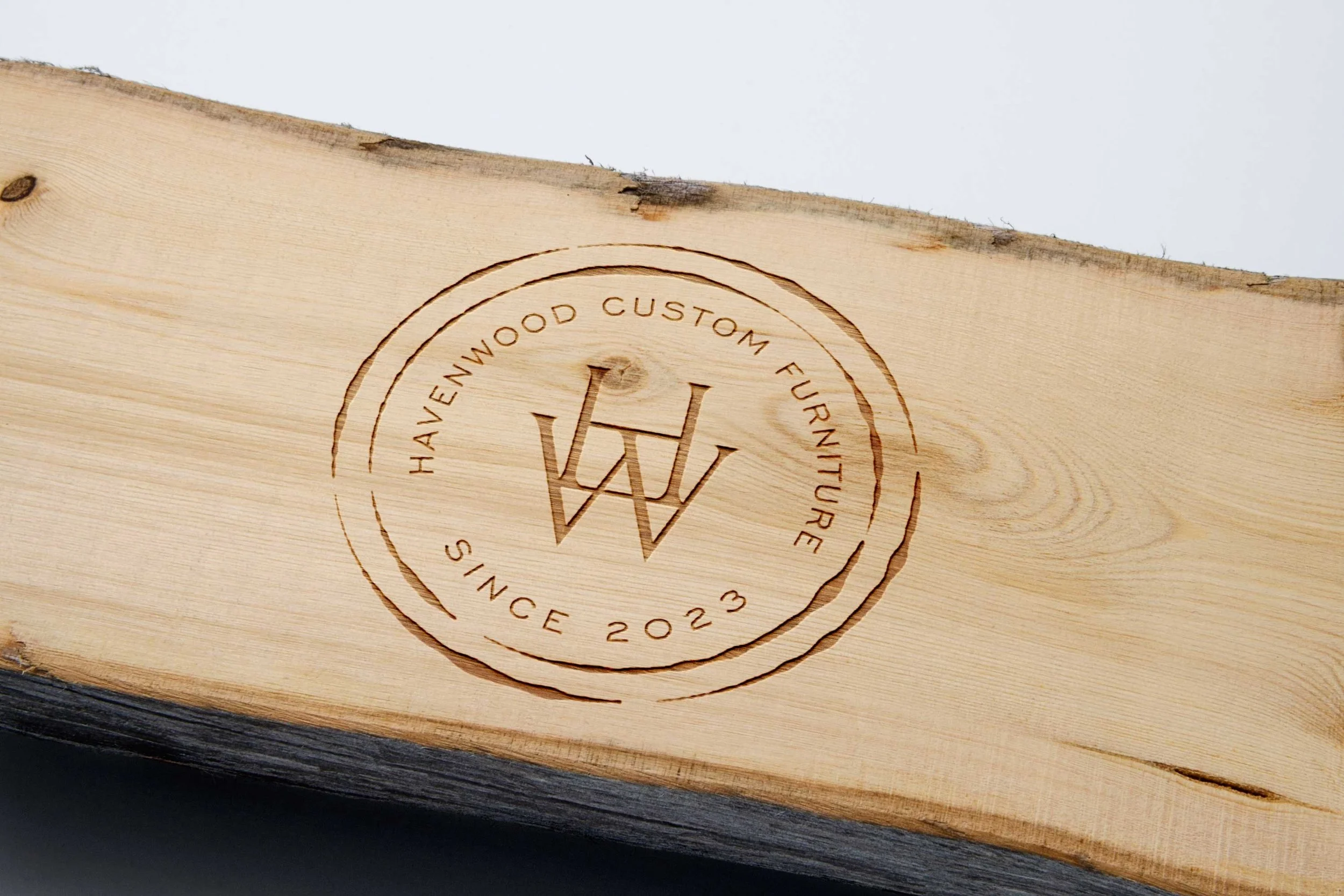 Engraved wood piece with a circular logo that reads 'Havenwood Custom Furniture Since 2023' surrounding a stylized 'HW' initials.