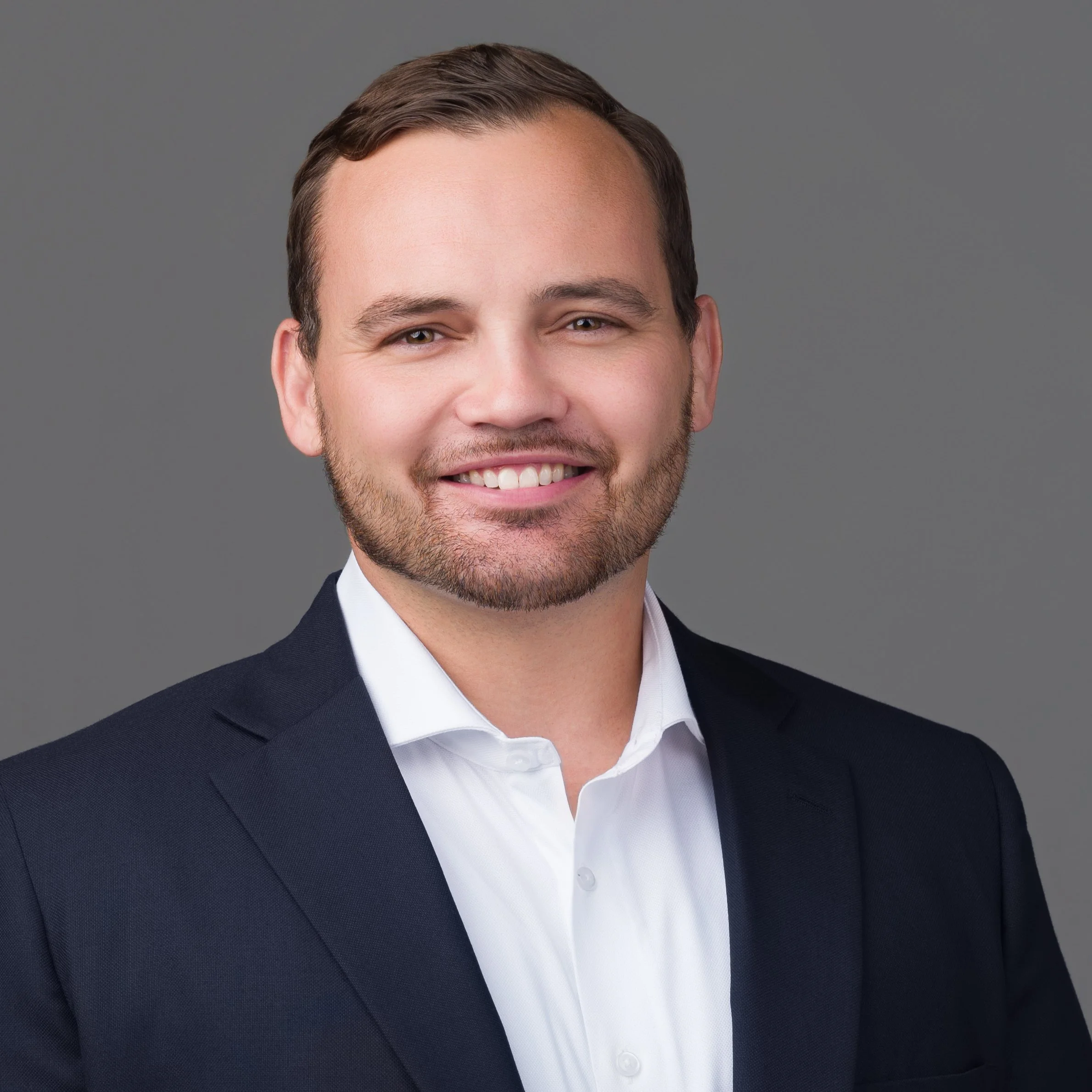 Portrait of a man with glasses wearing a black suit and white shirt against a white background.