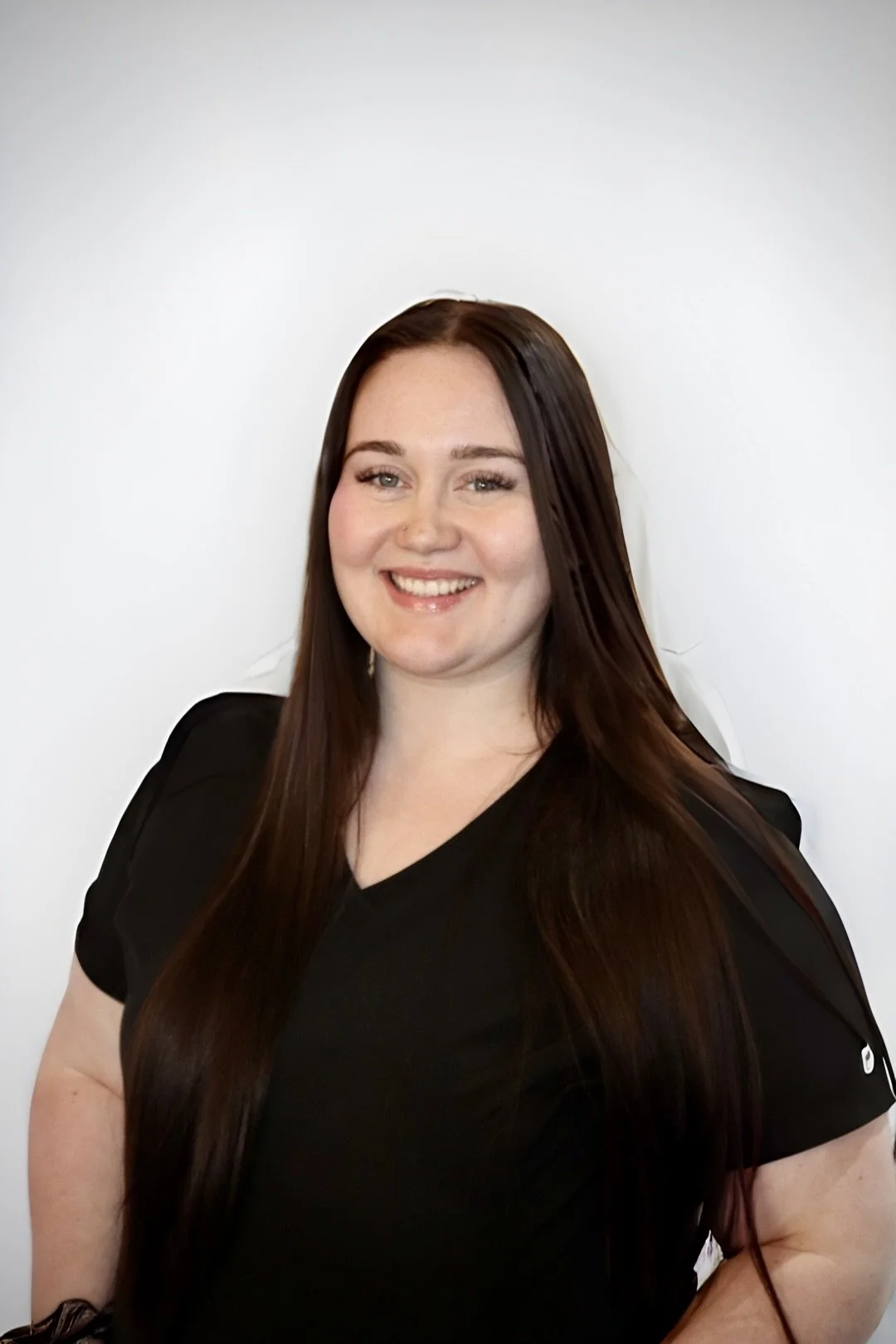 A smiling woman with long dark hair wearing a black top standing against a plain white background.
