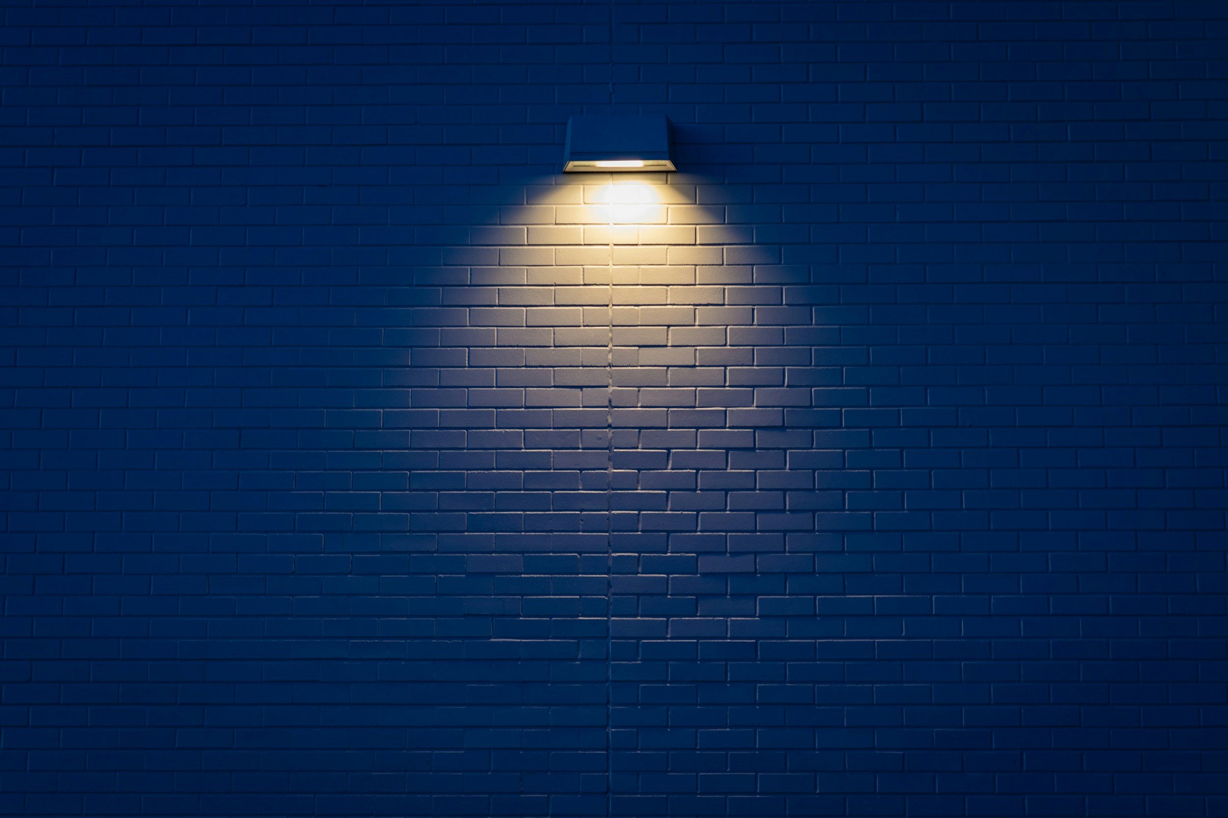 Eine Wand mit einer angebrachten Außenleuchte, die Licht auf die Ziegelsteine wirft.