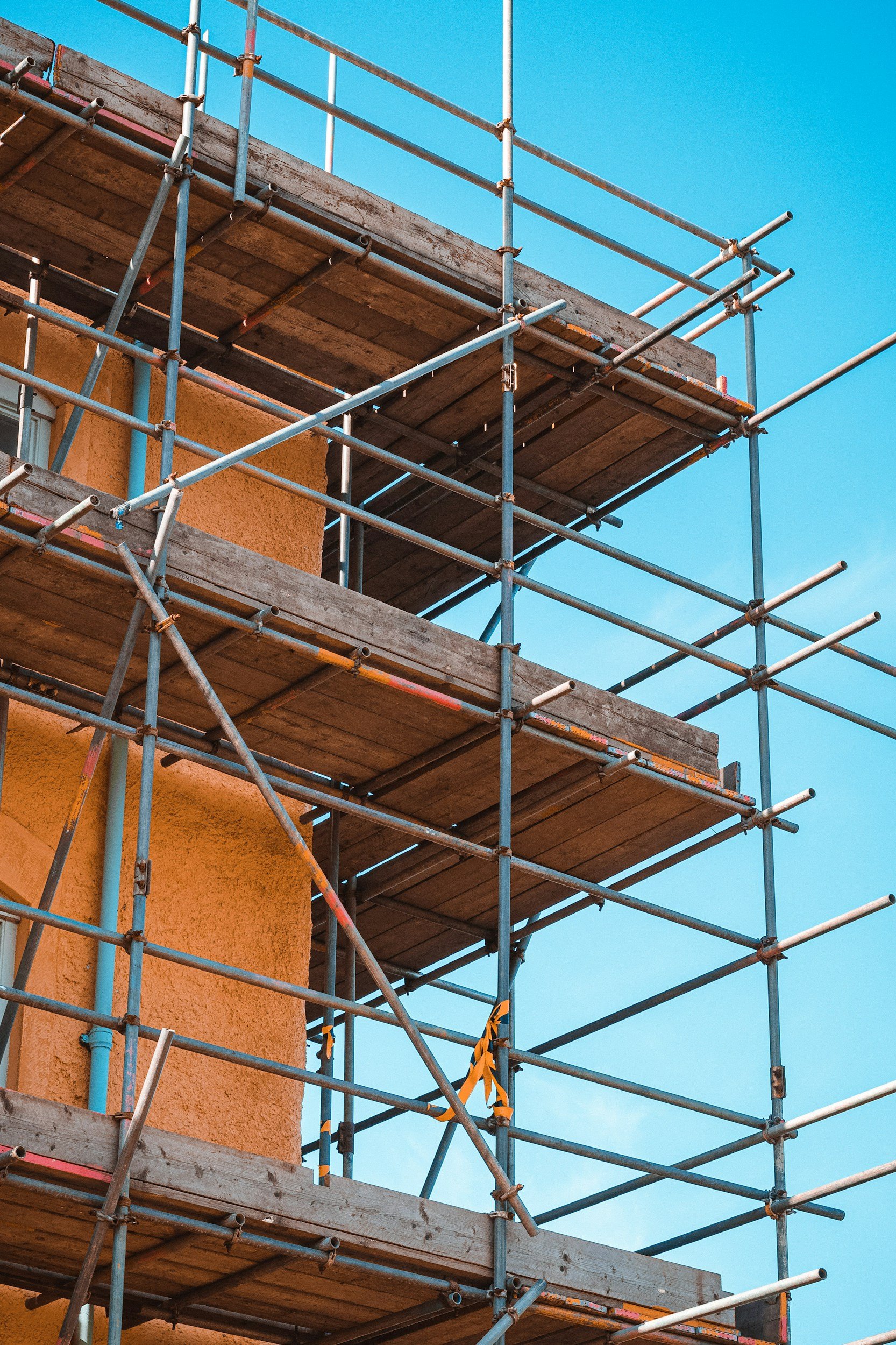 Gerüst um ein Gebäude, das mit orange Farbe gestrichen wird.