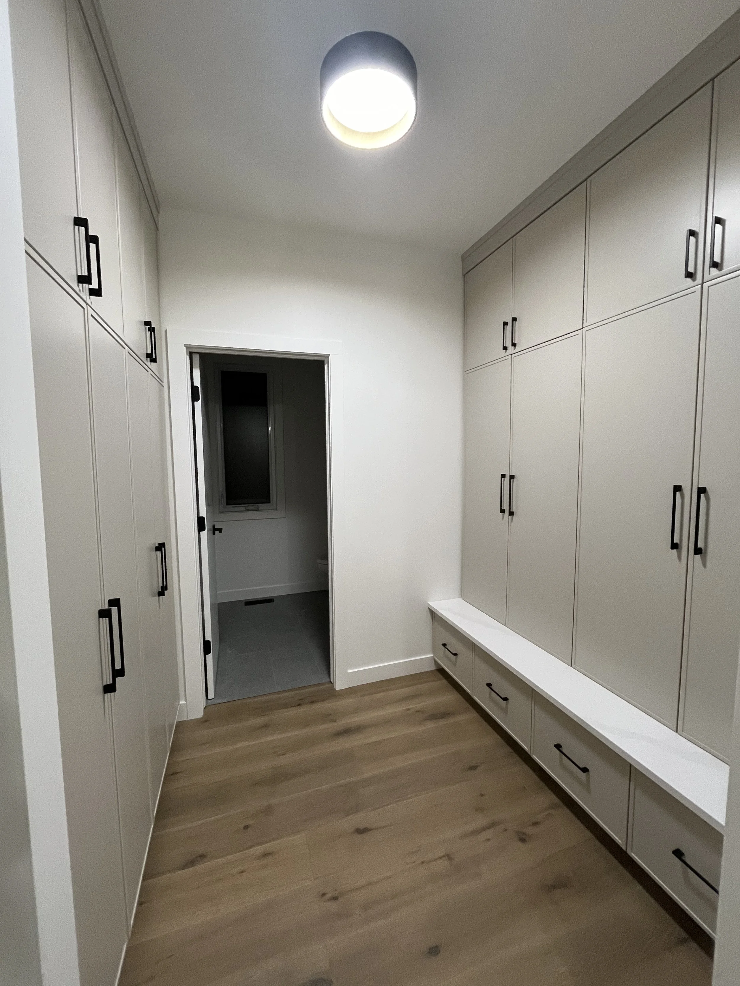 A walk-in closet with white cabinets, black handles, hardwood flooring, and a ceiling light fixture.
