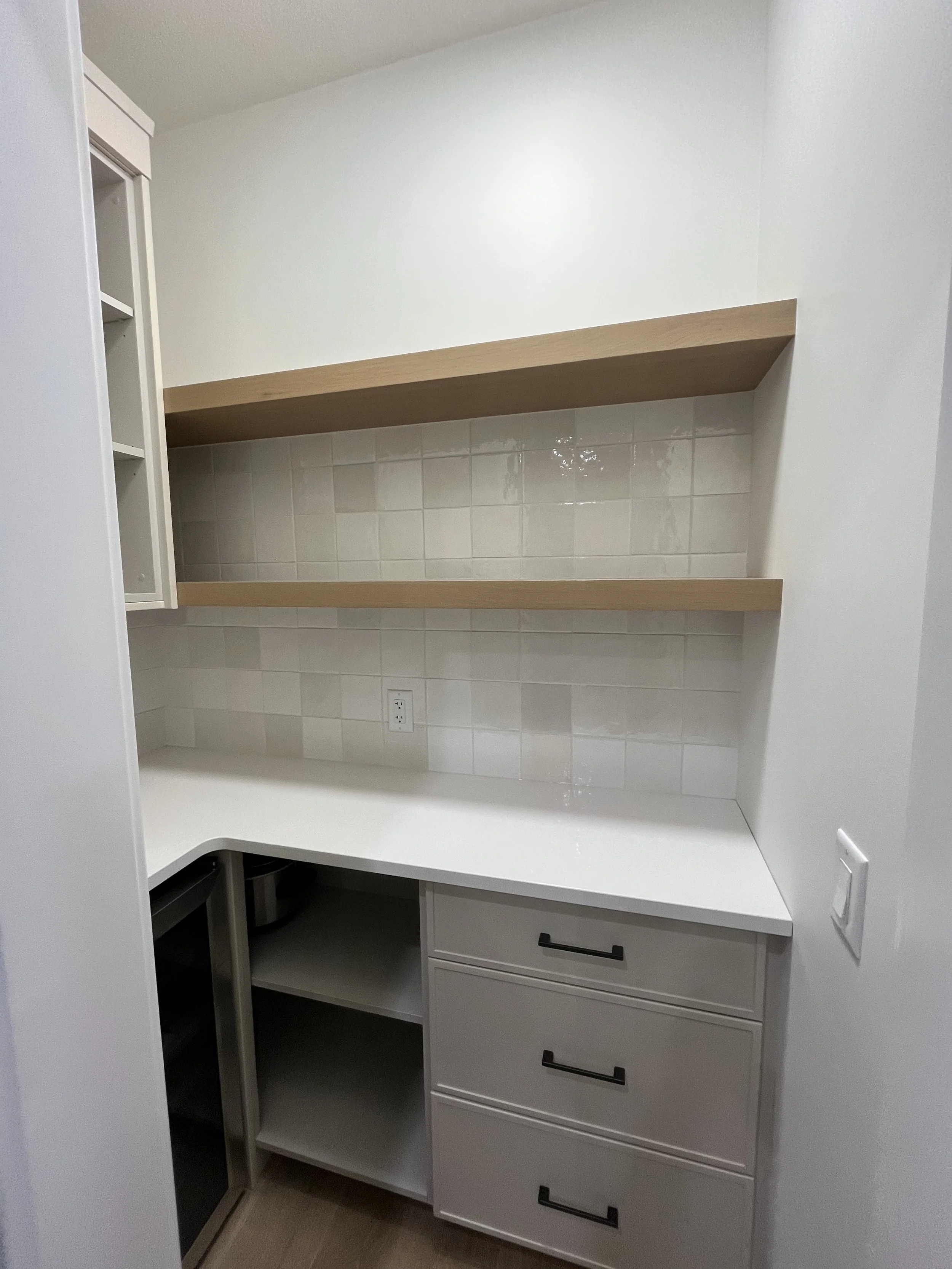 Empty kitchen corner with white cabinets, open shelving, tiled backsplash, and white countertop.