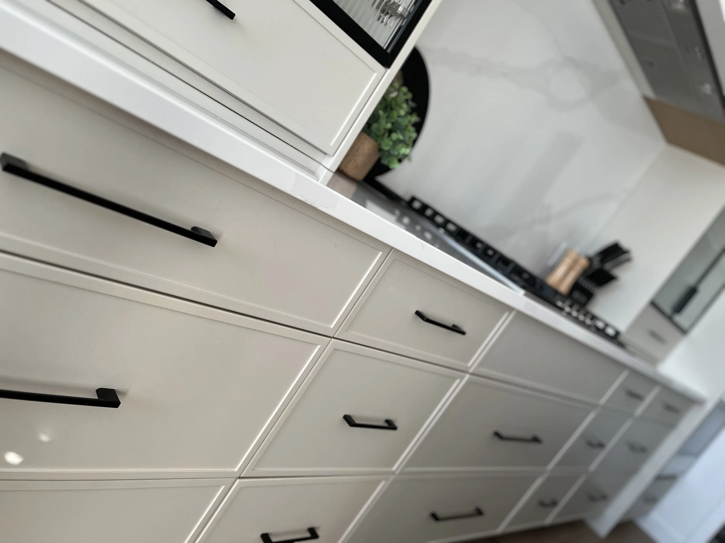 Modern kitchen with white cabinets, black handles, a white marble countertop, stove, and a potted plant.