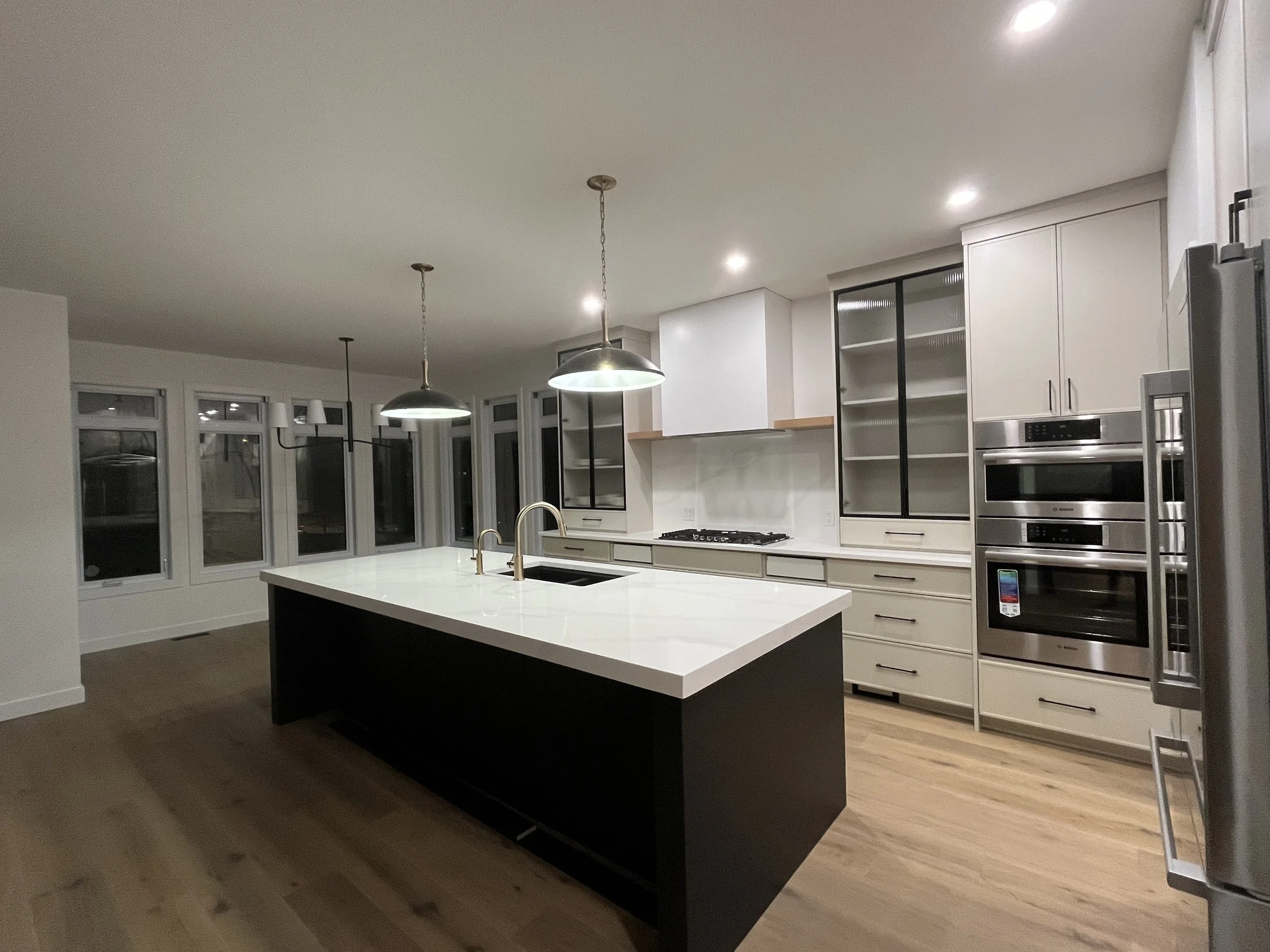 Modern kitchen with white cabinets, stainless steel appliances, a large island with a white countertop, and pendant lighting overhead.