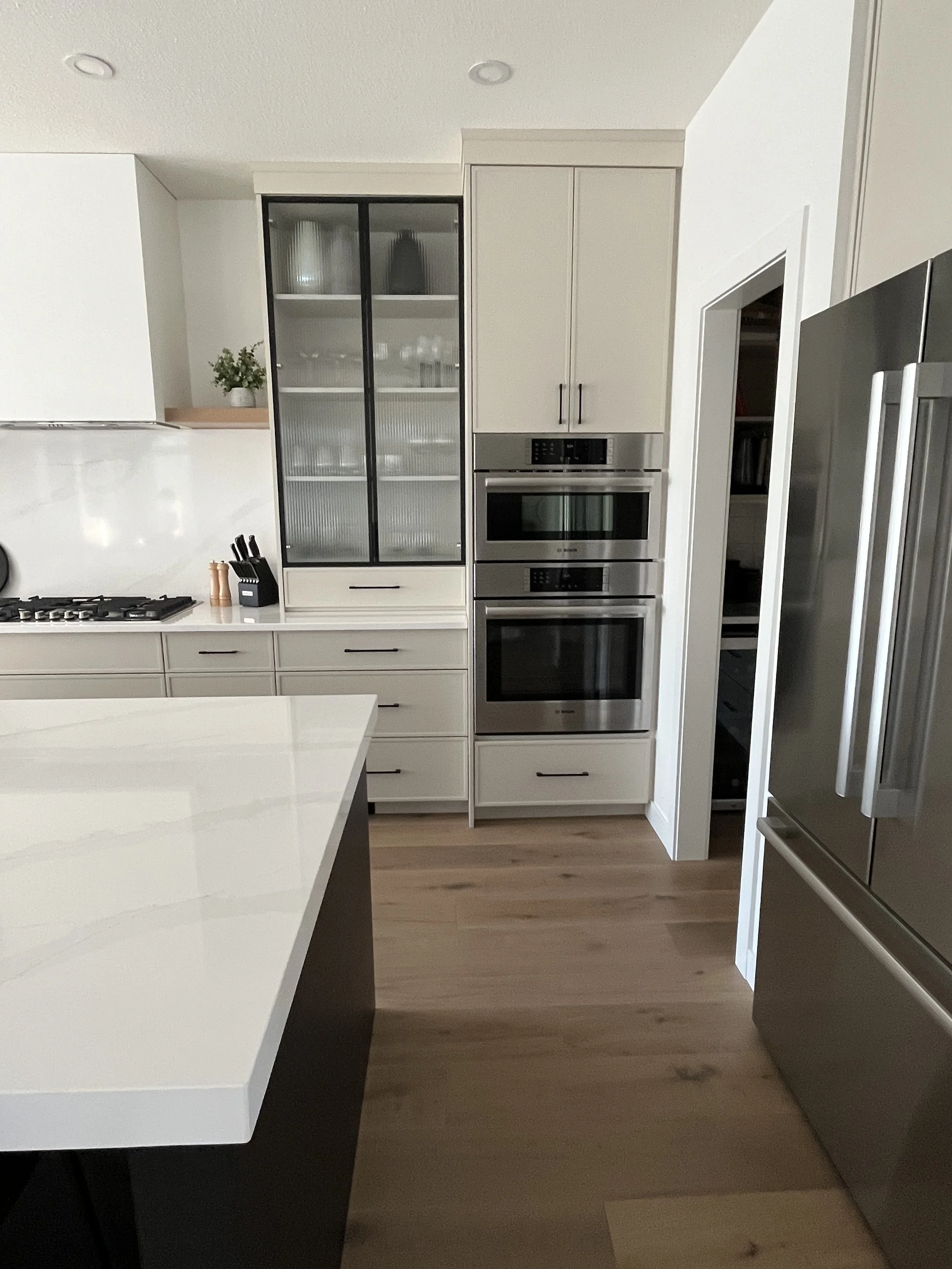 Modern kitchen with white cabinets, stainless steel appliances, a black and glass display cabinet, and light wood flooring.