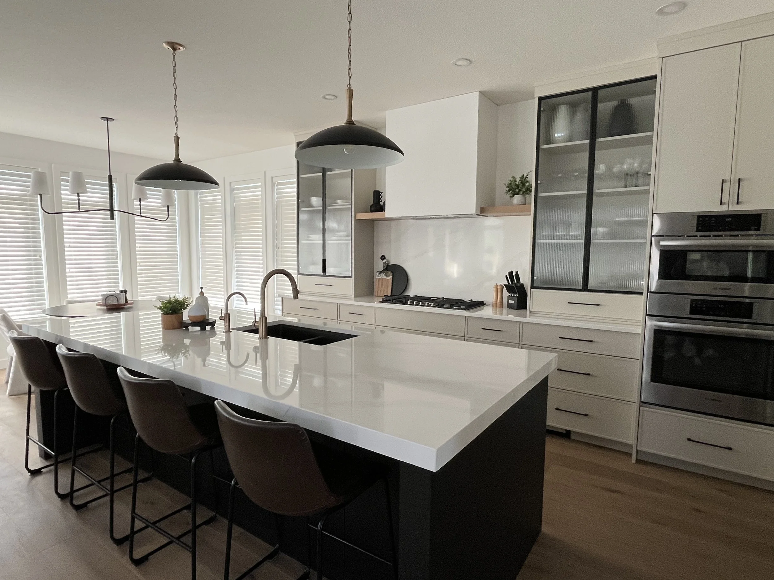 Modern kitchen with white cabinetry, black and bronze fixtures, a large white island with seating, and stainless steel ovens.