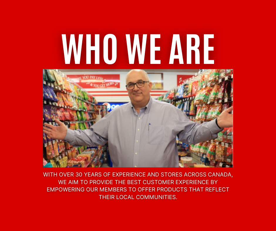 A man in glasses and a light gray shirt standing in an aisle of a grocery or convenience store with his arms outstretched, surrounded by shelves filled with snack items.