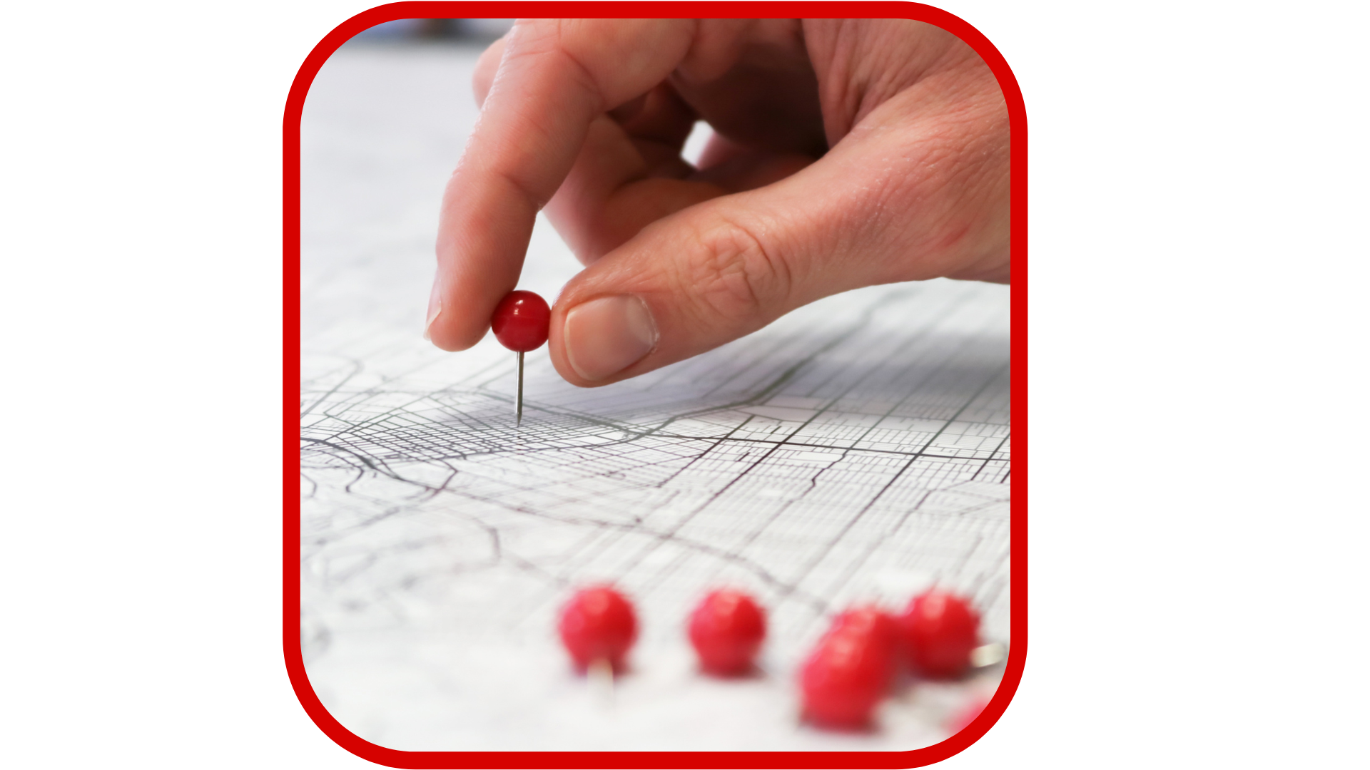 Close-up of a person's hand placing a red pushpin into a detailed map or blueprint with multiple lines and grids, with several other red pushpins in the foreground.