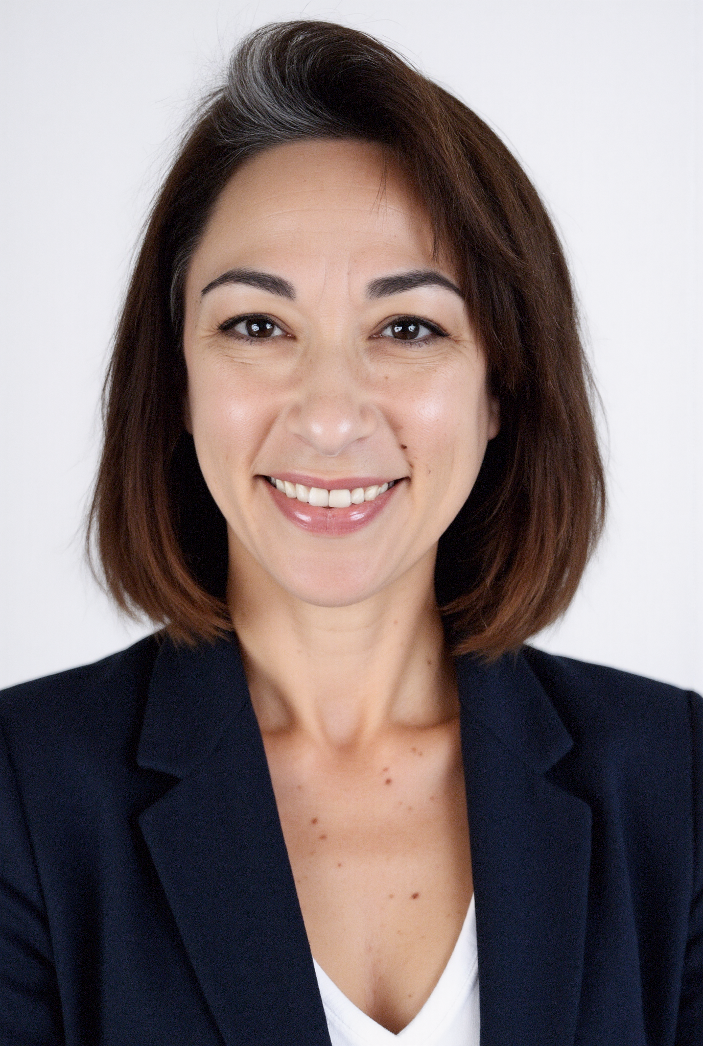 A professional woman with shoulder-length dark hair, smiling, wearing a navy blazer and white blouse, against a plain white background.