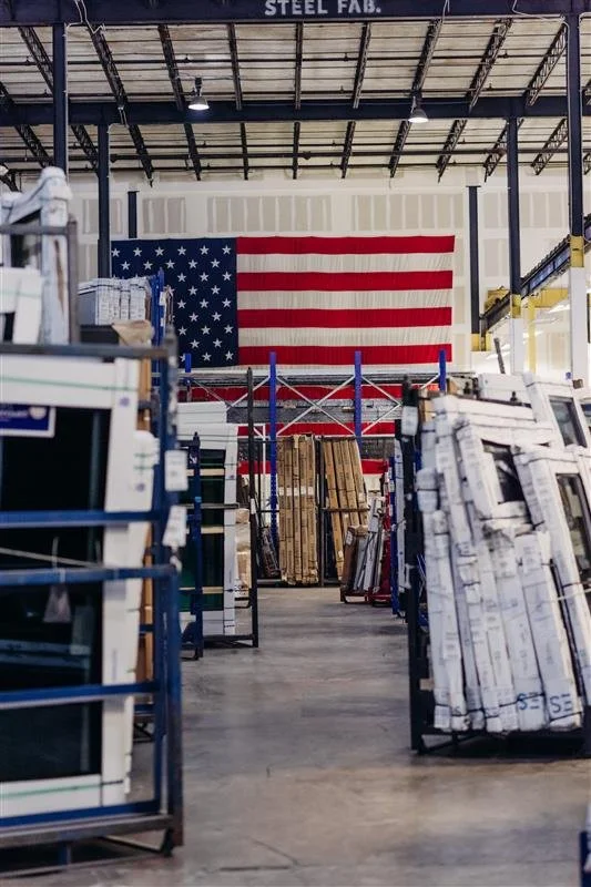American flag hanging inside a warehouse with shelves of construction materials and windows.