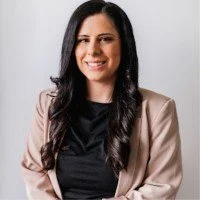 Professional woman with long dark hair, wearing a tan blazer over a black top, smiling against a plain background.