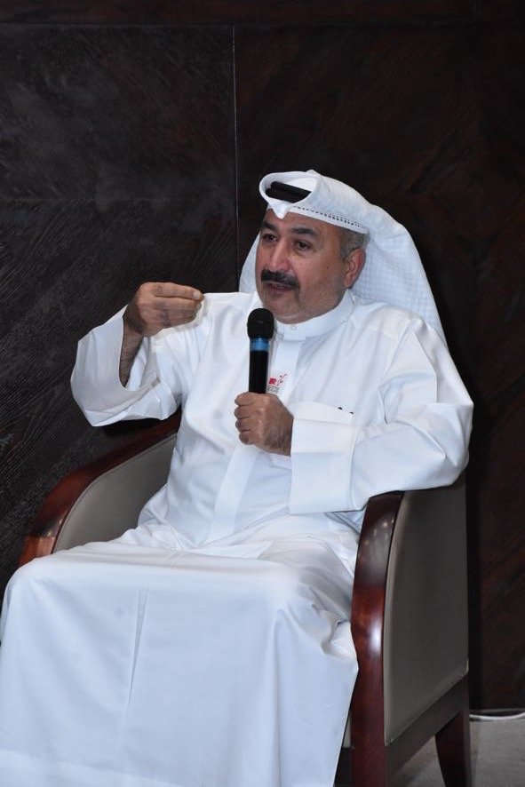 Man wearing traditional Middle Eastern attire, including a white thobe and head covering, sitting in a chair and speaking into a microphone.