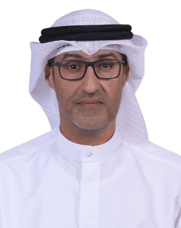 A man wearing traditional Middle Eastern attire, including a white kandura, a white headscarf (ghutra), and a black agal, with glasses and a neutral expression.