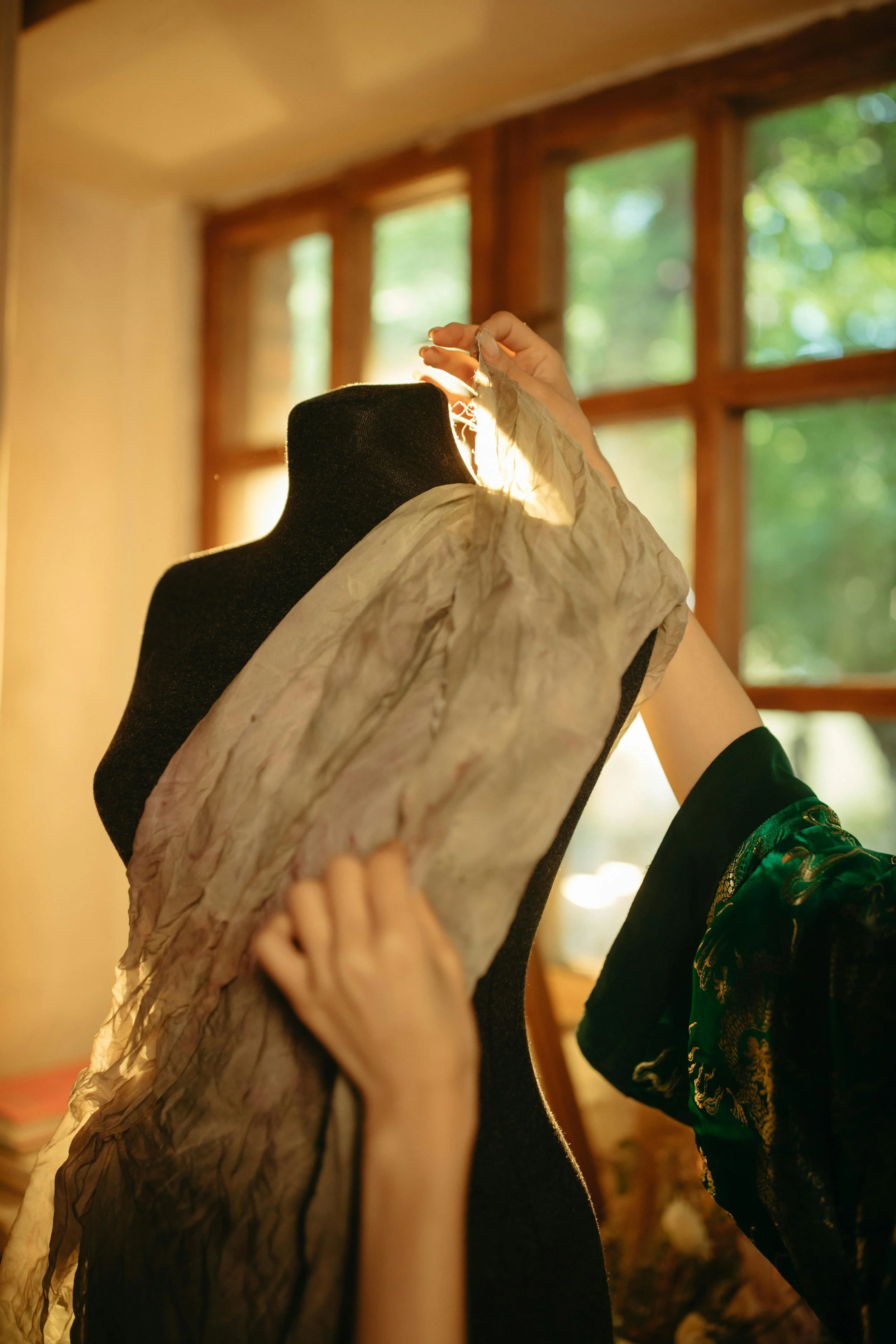Une personne ajuste un tissu sur un mannequin de couture, baignée par la lumière naturelle d’un atelier chaleureux. Cette image évoque l’inspiration créative, l’artisanat et la passion du stylisme fait main.
