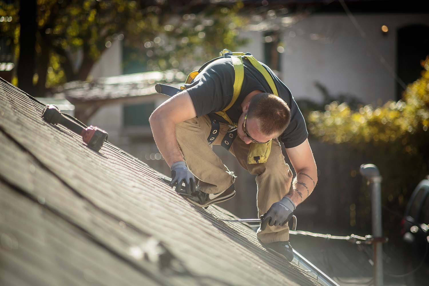 Professional roofing contractor wearing a safety harness while inspecting a shingle roof to provide roof leak repair services.