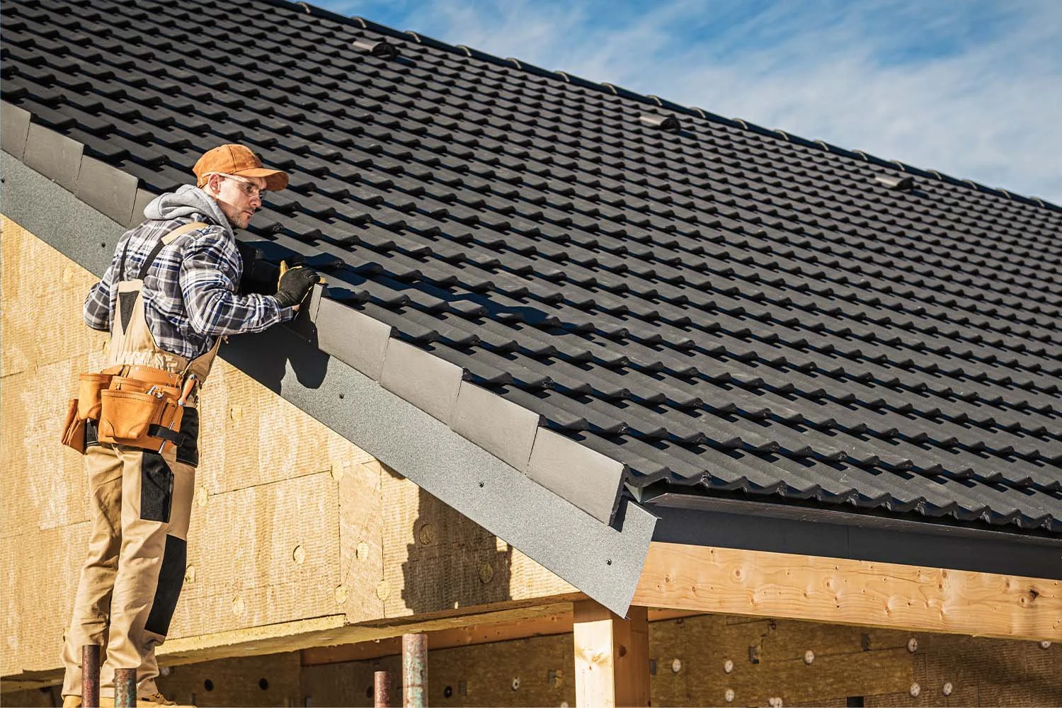 Professional roofer with a toolbelt installing dark modern tiles on a residential home to provide a permanent leaking roof fix.