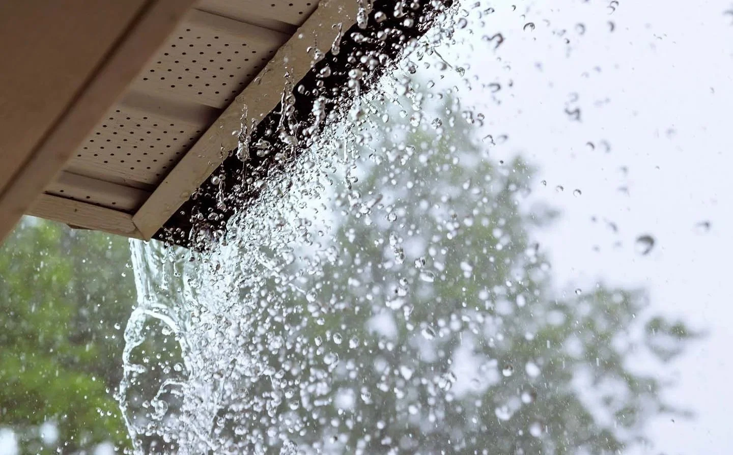 Heavy rain pouring down from a roof edge without a rain gutter guard installed, showing why homeowners ask what are gutter guards.