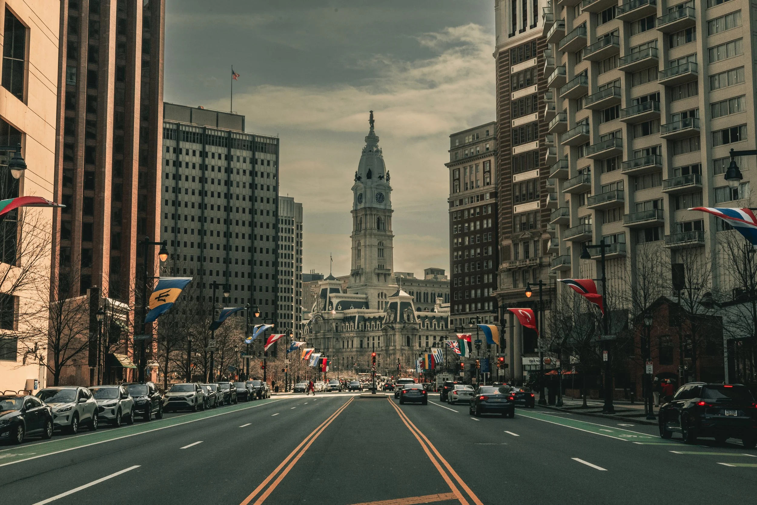 Street view of Philadelphia City Hall with tall buildings and flags lining the road