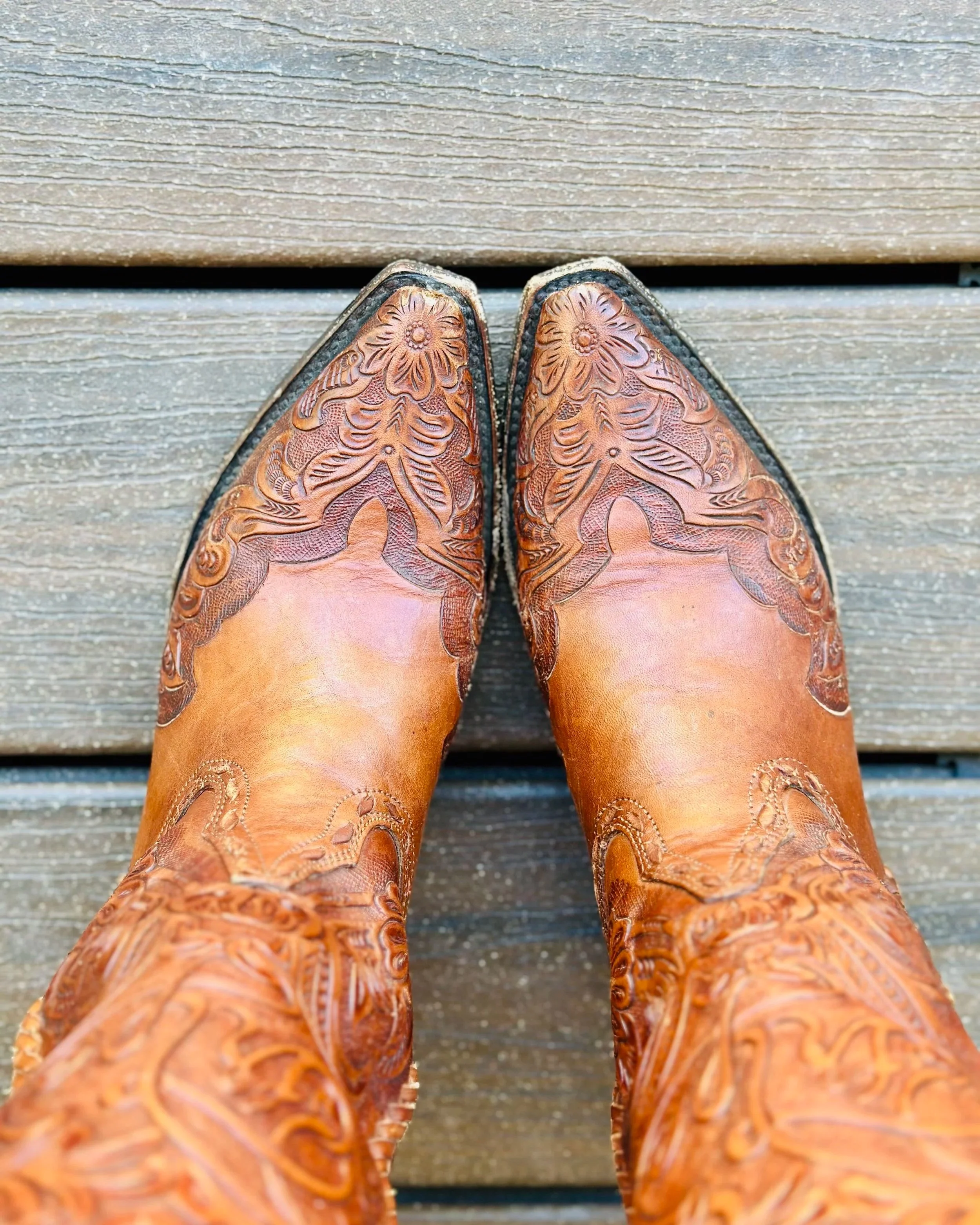 Close-up of brown embroidered cowboy boots resting on a wooden deck.