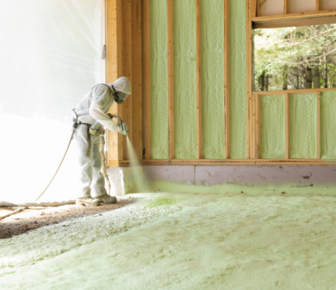 Worker spray-foaming an interior wall of a building under construction.