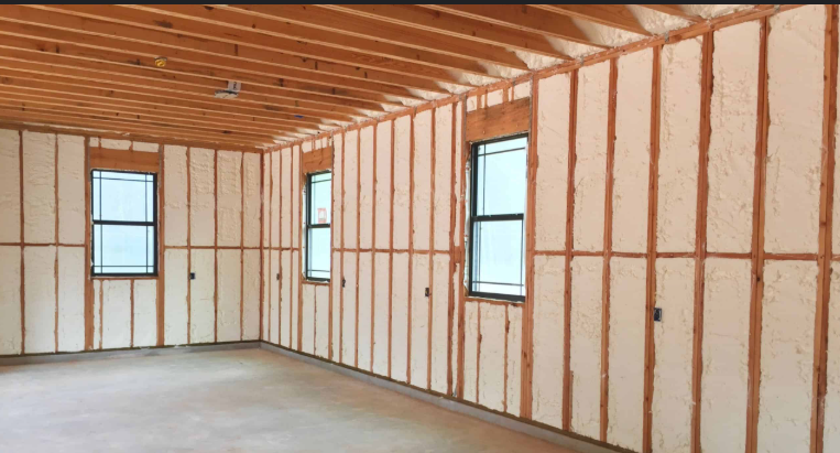 Interior of a house under construction with insulated walls, wooden studs, and three windows.