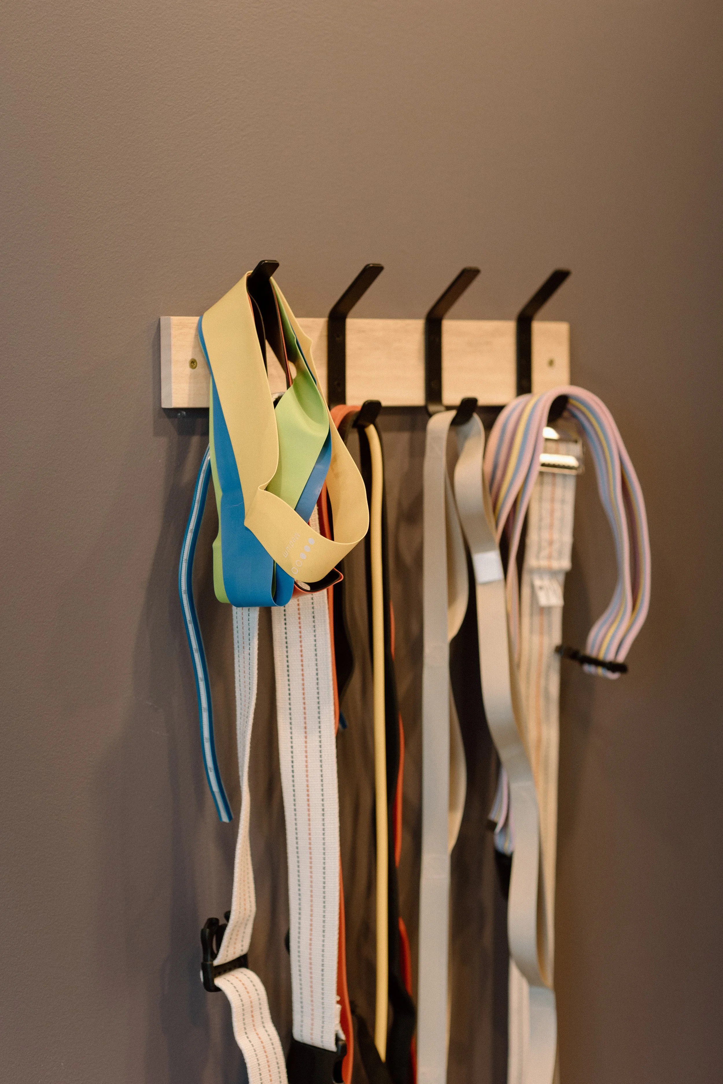A wall-mounted wooden rack with hooks holding colorful belts and straps.