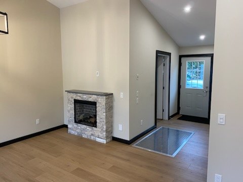 Empty living room with a fireplace, hardwood floors, and a front door with a screen door.