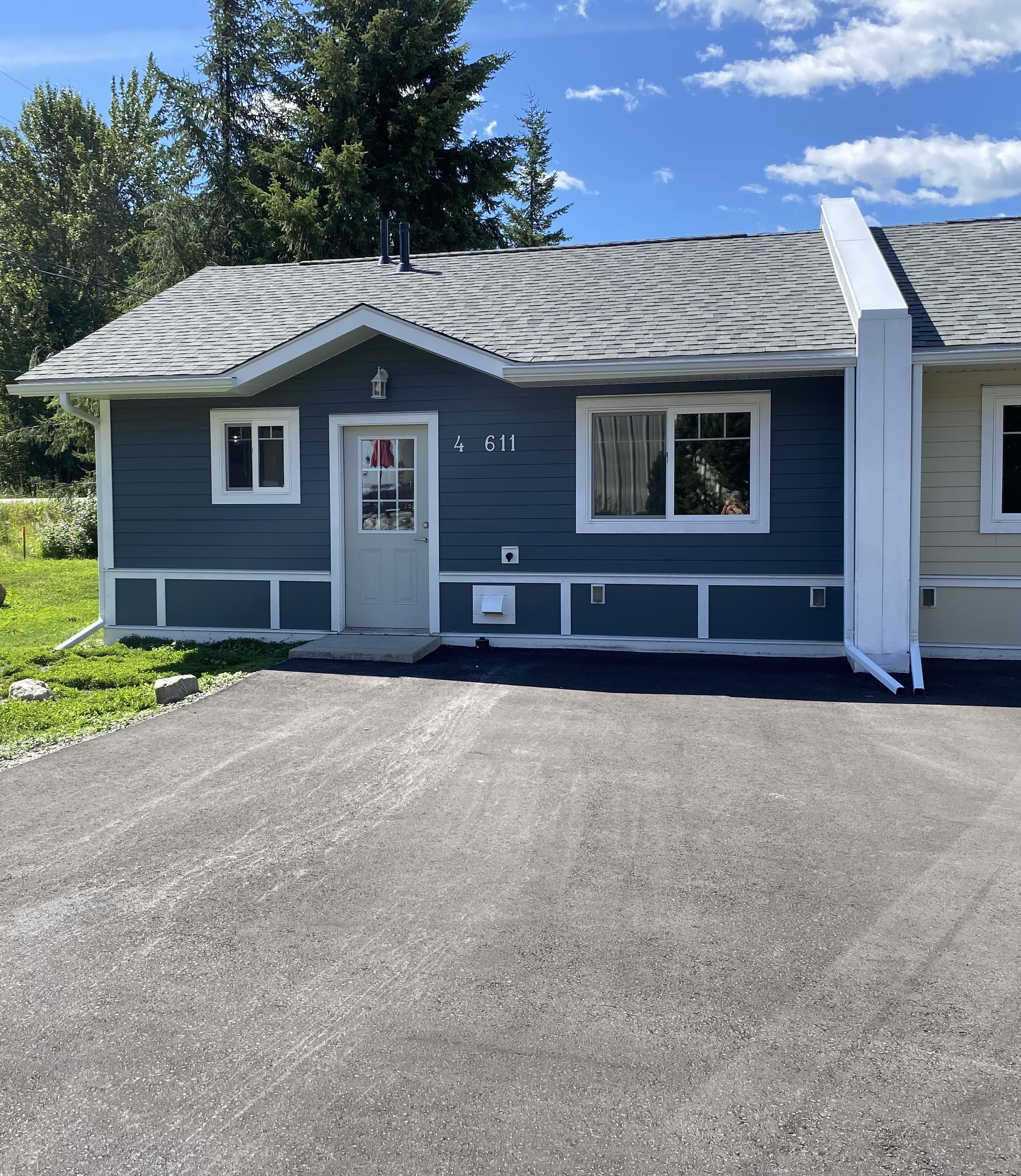 Exterior of a blue house with white trim, two small front steps, and a black driveway under a partly cloudy sky.