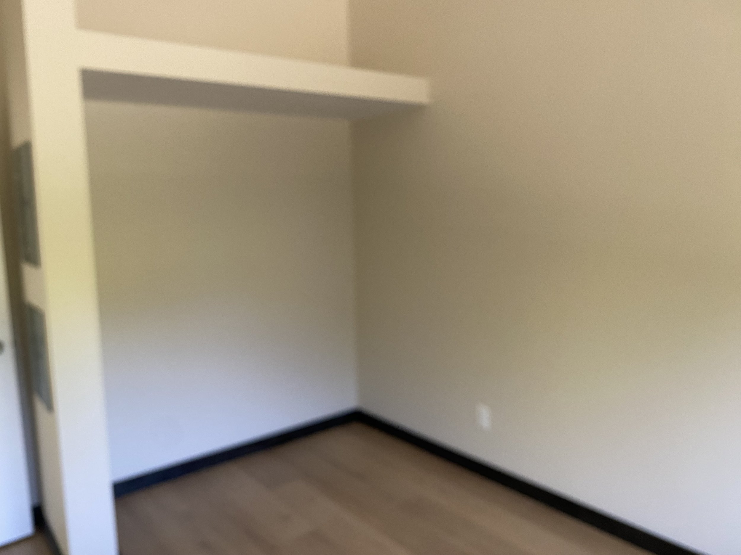 Empty room with beige walls, black baseboard, and light wood floor.