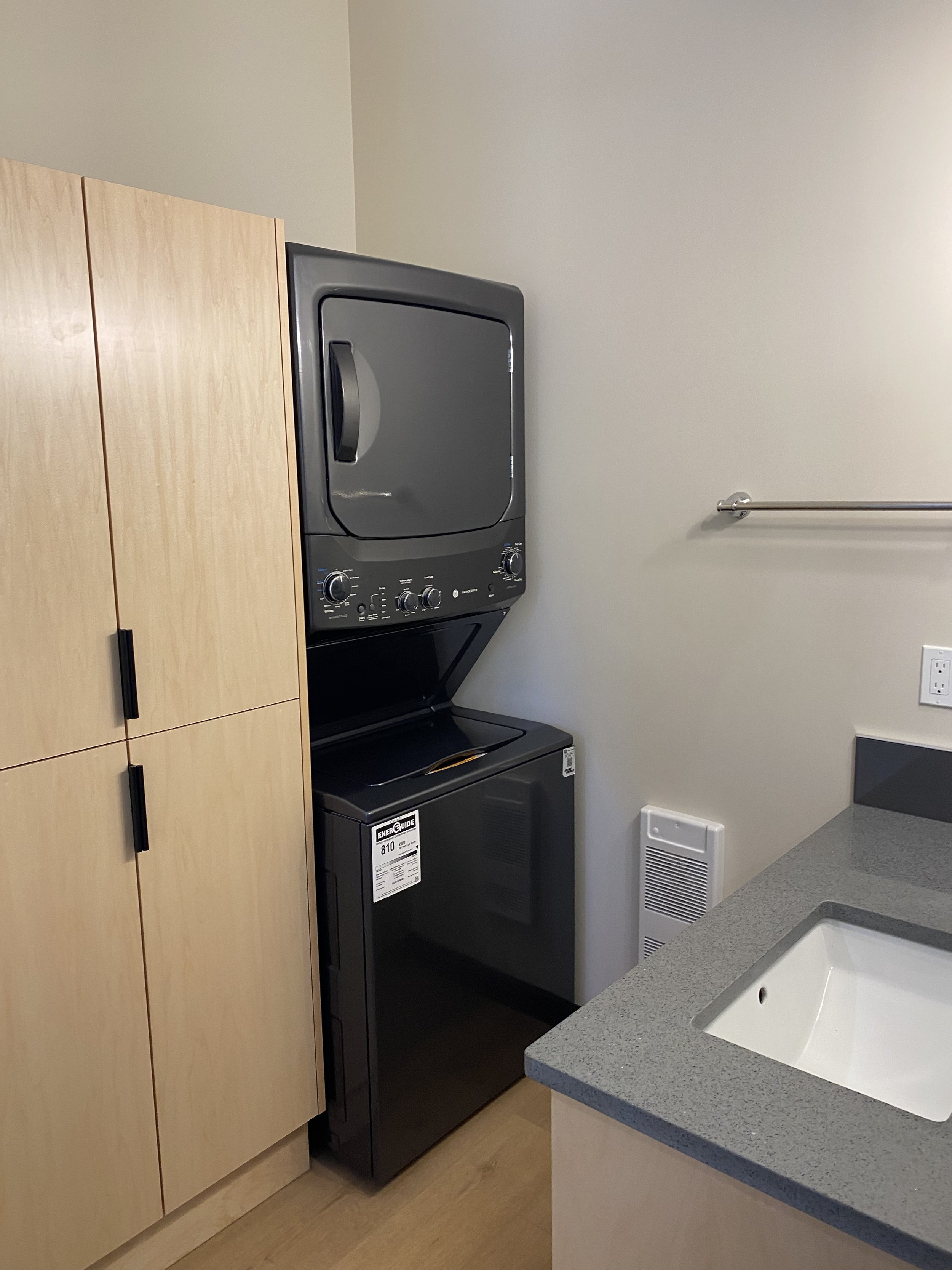 Laundry area with stacked washer and dryer, wooden cabinets, and a granite countertop with a sink.
