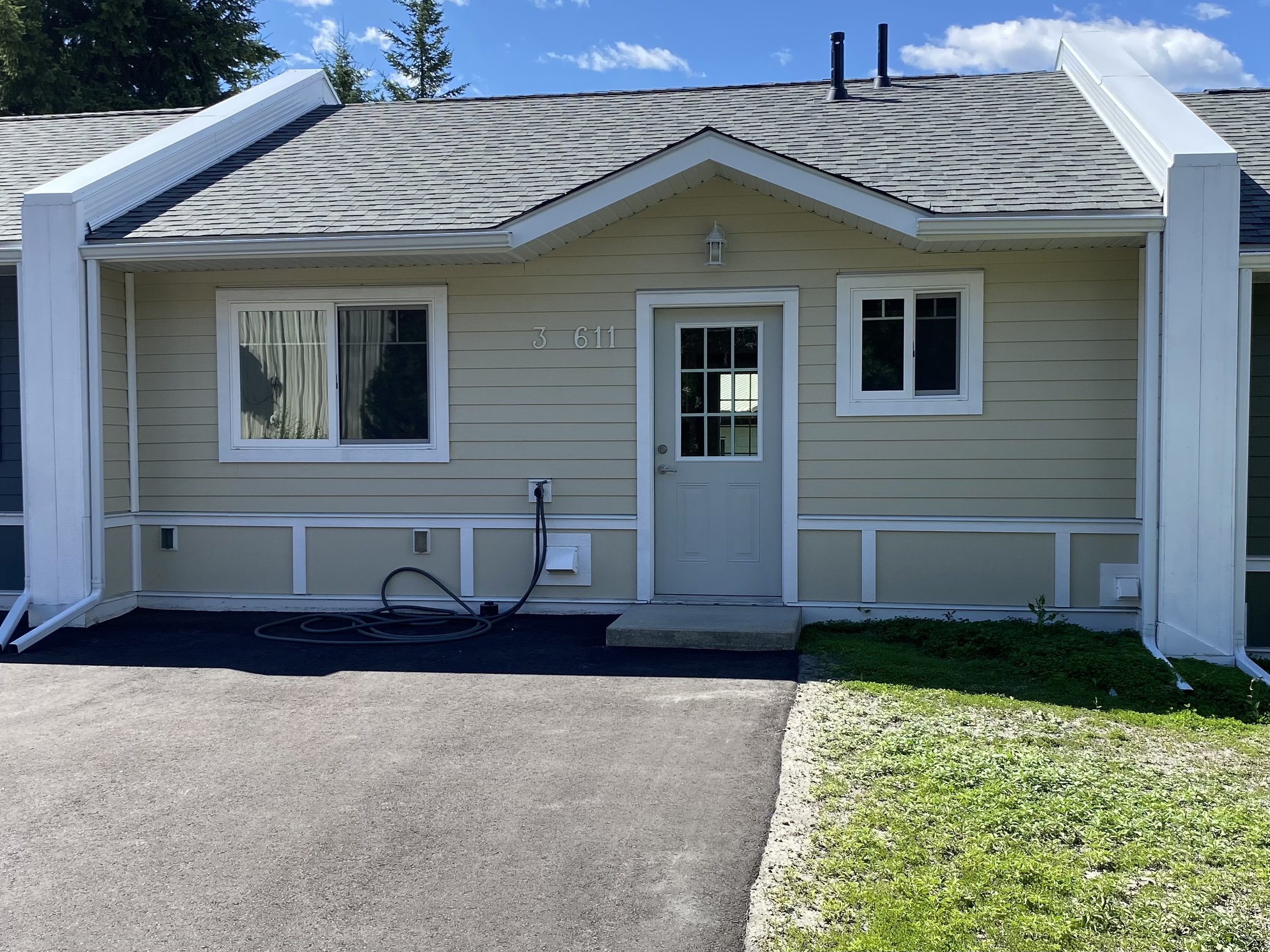 Front view of Creekside Villas, a light yellow house with white trim, two windows, and a door, with a paved driveway and a small grassy area.