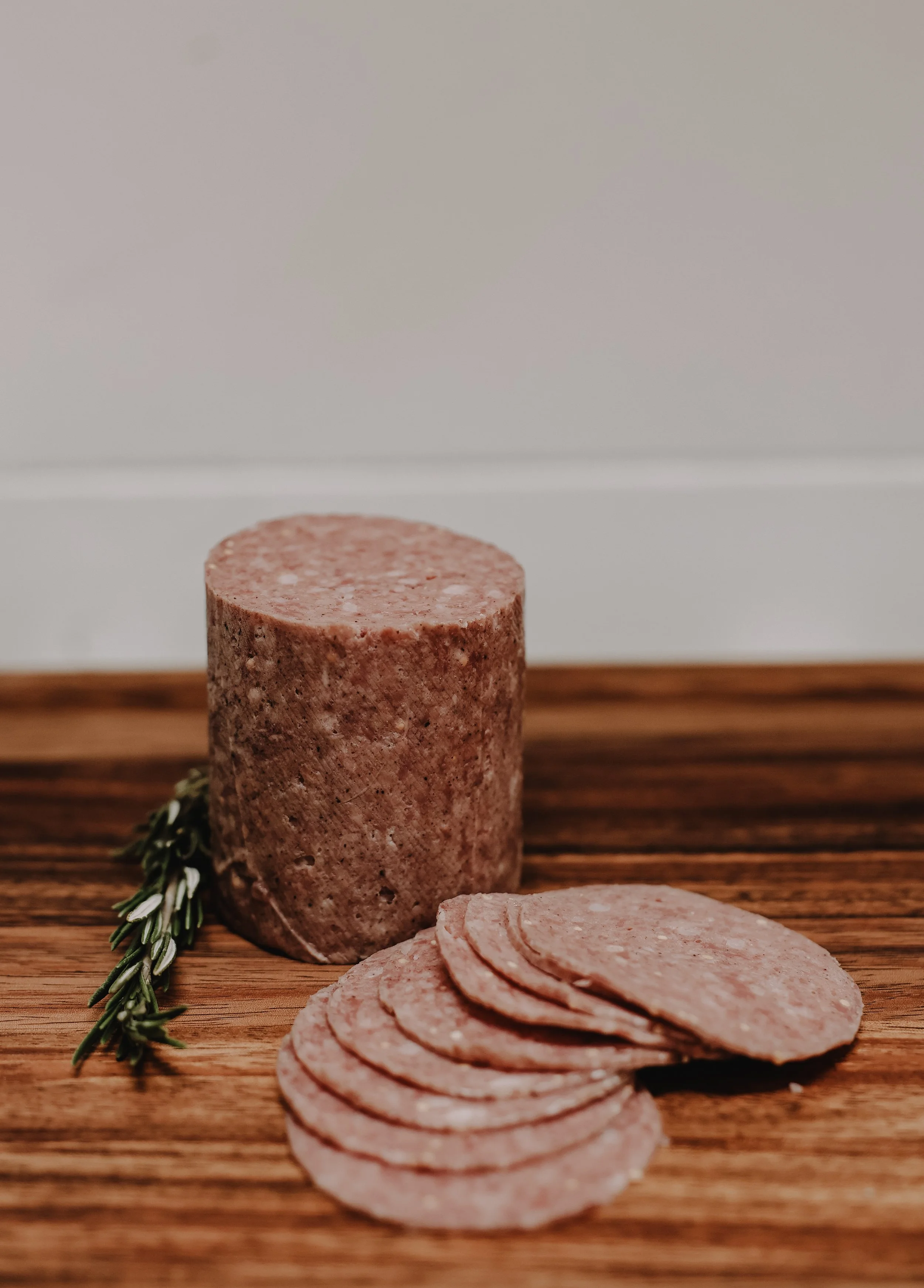 Sliced sausage and a sprig of rosemary on a wooden surface.
