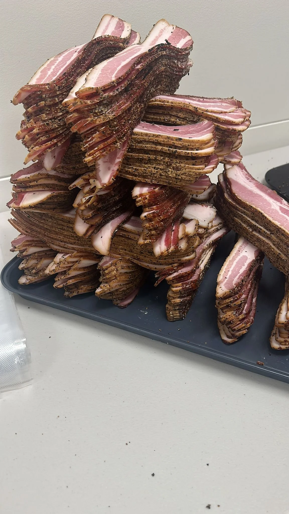 Stacked slices of raw bacon on a gray tray.