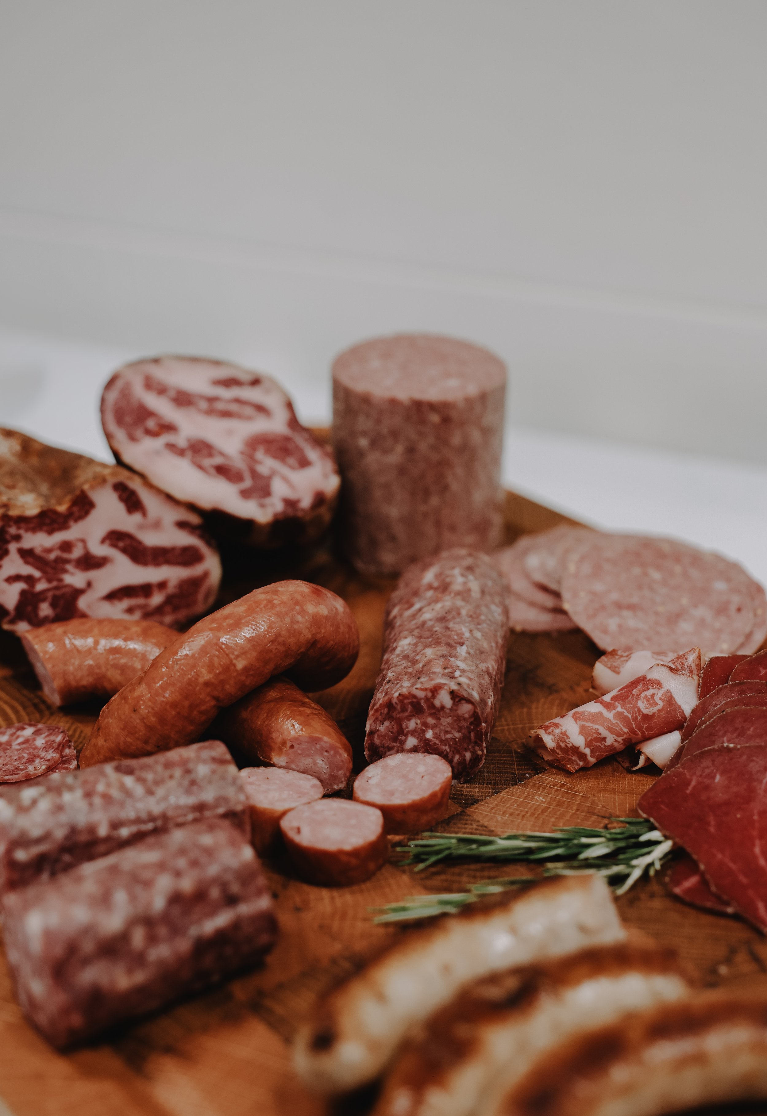 Assorted sliced and whole cured meats on a wooden board, including sausages, salami, and prosciutto.