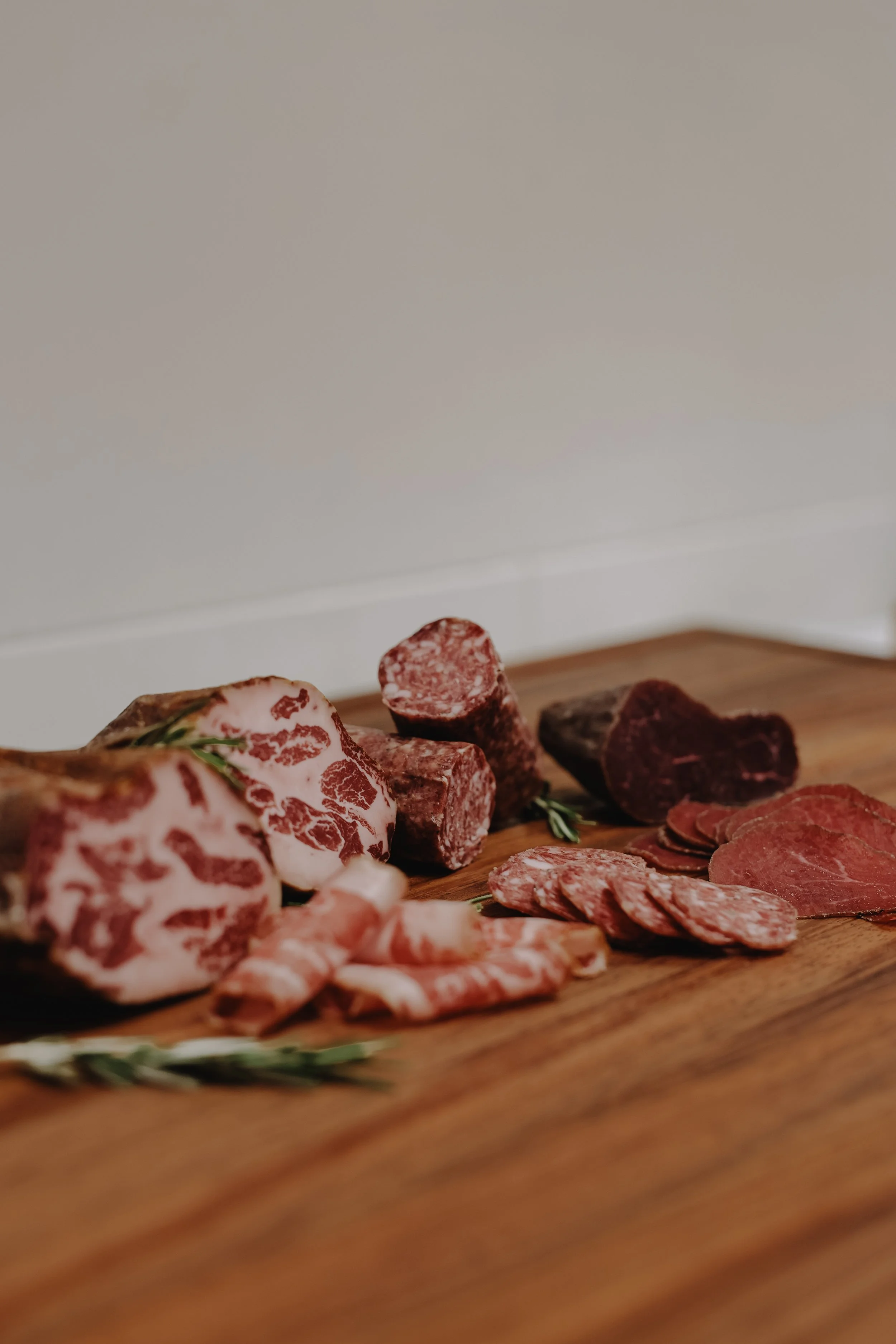 Assorted cured meats and salami on a wooden platter, garnished with sprigs of rosemary.