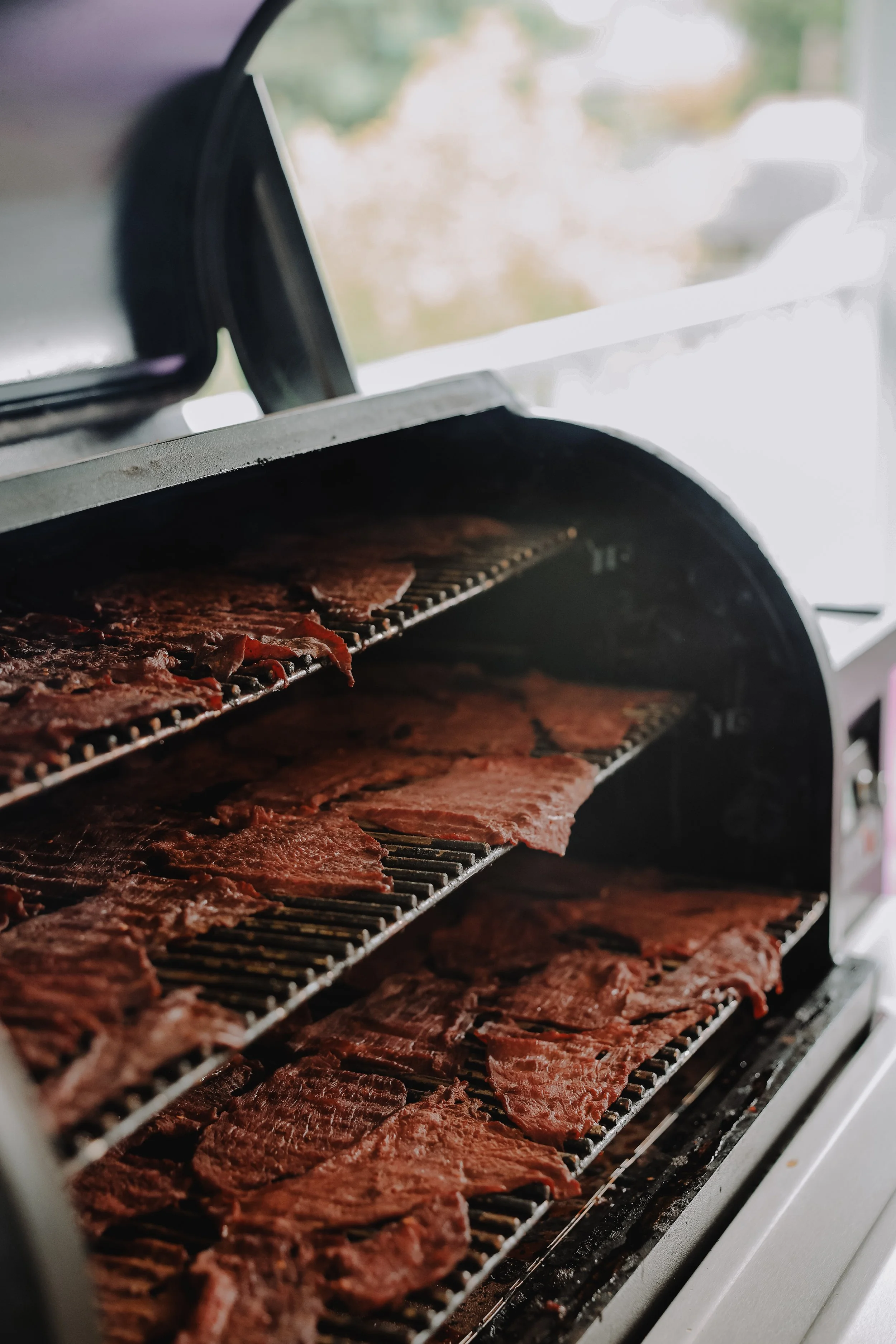 Slices of raw meat on a rotisserie grill inside a smoker