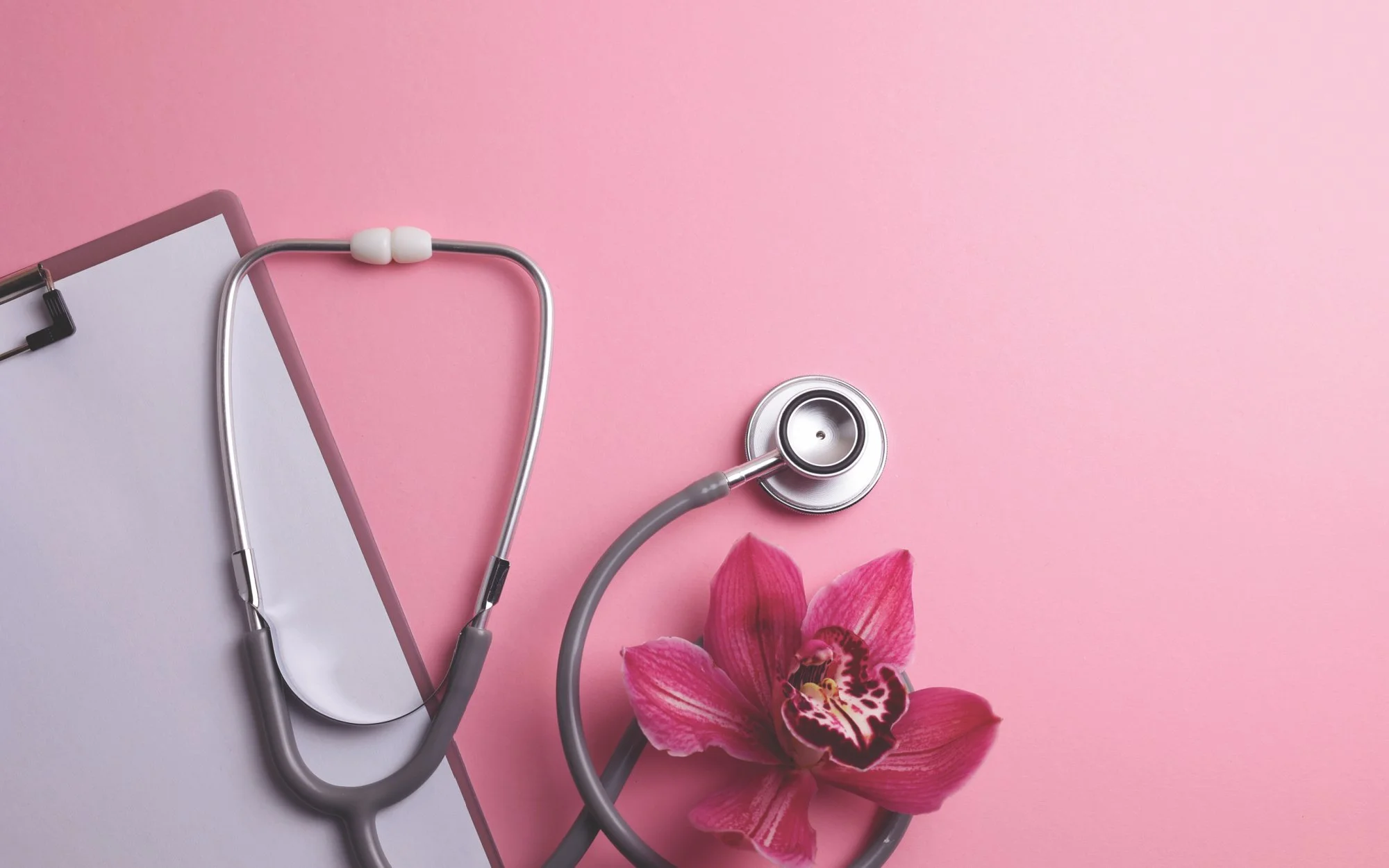 Medical stethoscope, pink orchid flower, clipboard, and eye chart on a pink background.
