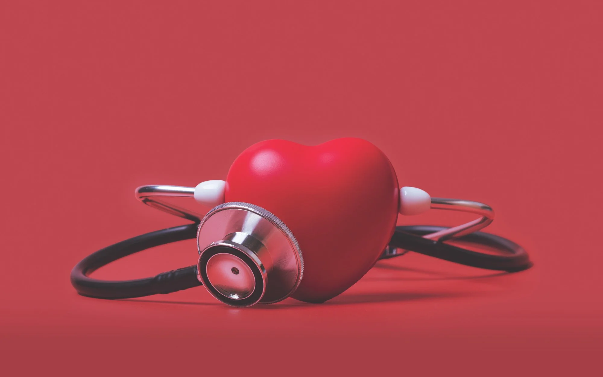 A stethoscope and a red heart-shaped object placed on a red background.