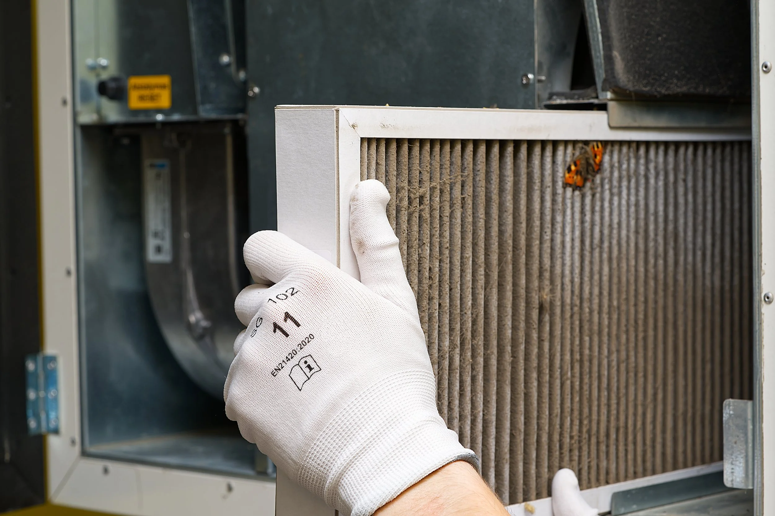 A person wearing white gloves installing or replacing an air filter in a heating, ventilation, and air conditioning (HVAC) system.