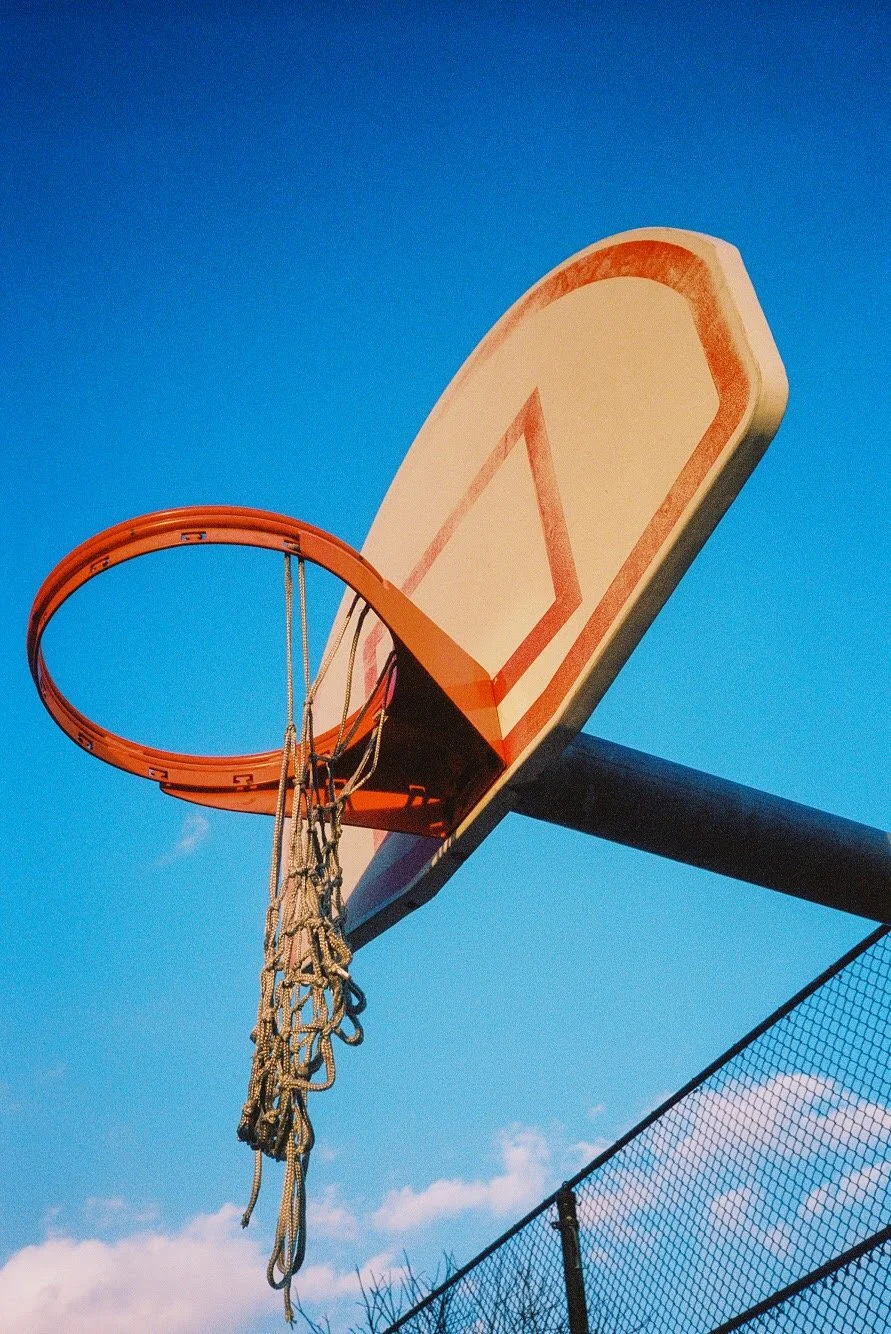 An outdoor basketball hoop mounted on a pole against a blue sky with some clouds.