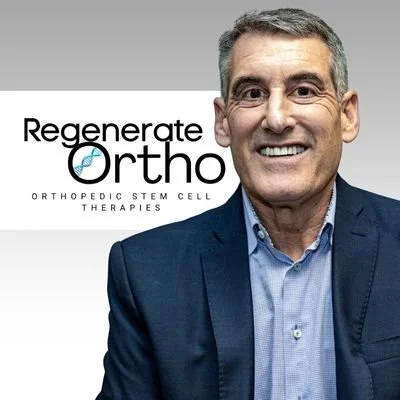 A man in a blue suit smiling standing in front of a sign that reads 'Regenerate Ortho Orthopedic Stem Cell Therapies'