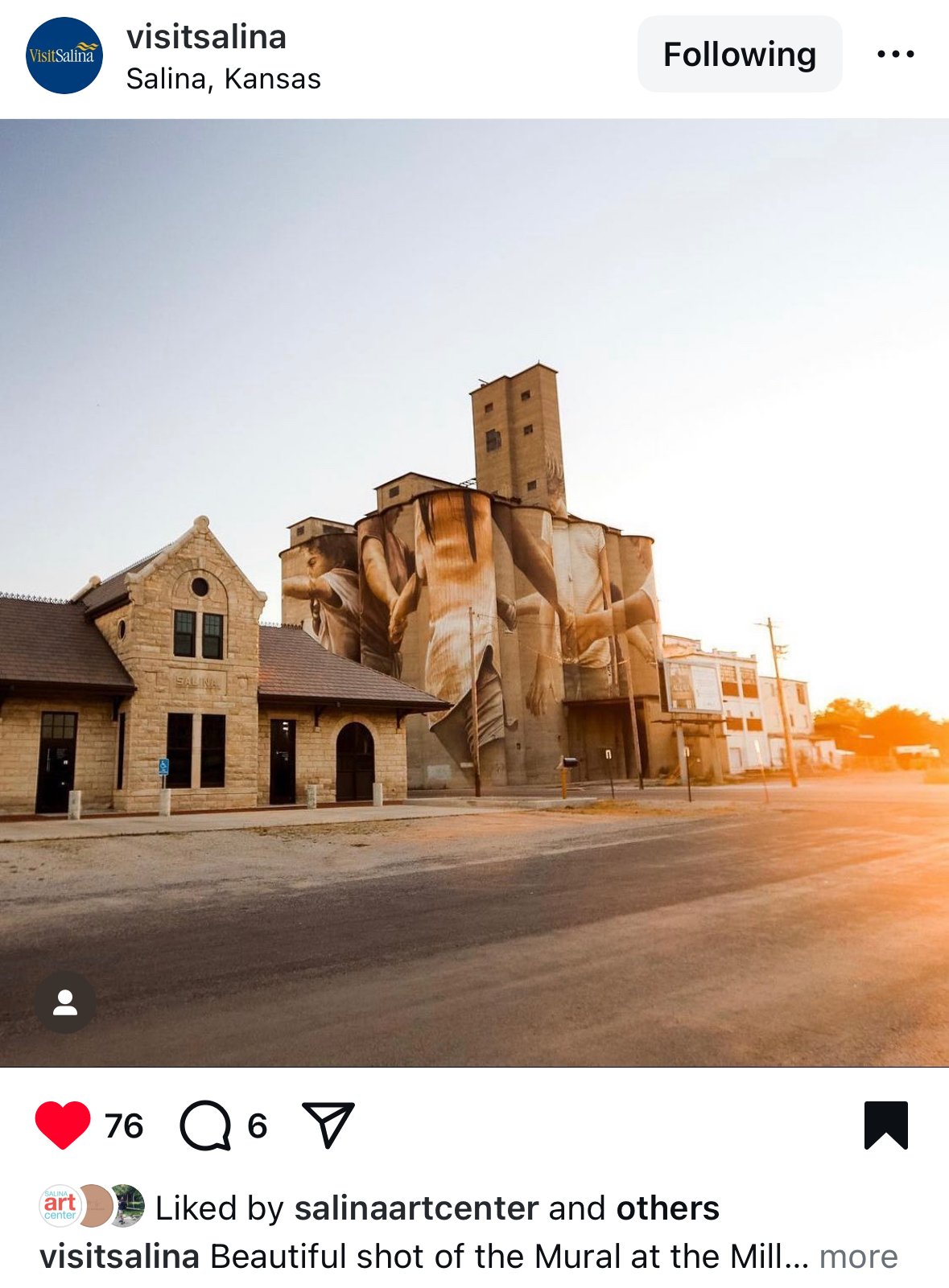 A mural on the side of a historic building in Salina, Kansas, depicting large human figures in a sepia tone. The mural covers multiple cylindrical silos, blending modern art with the industrial architecture of a mill, during a sunset.