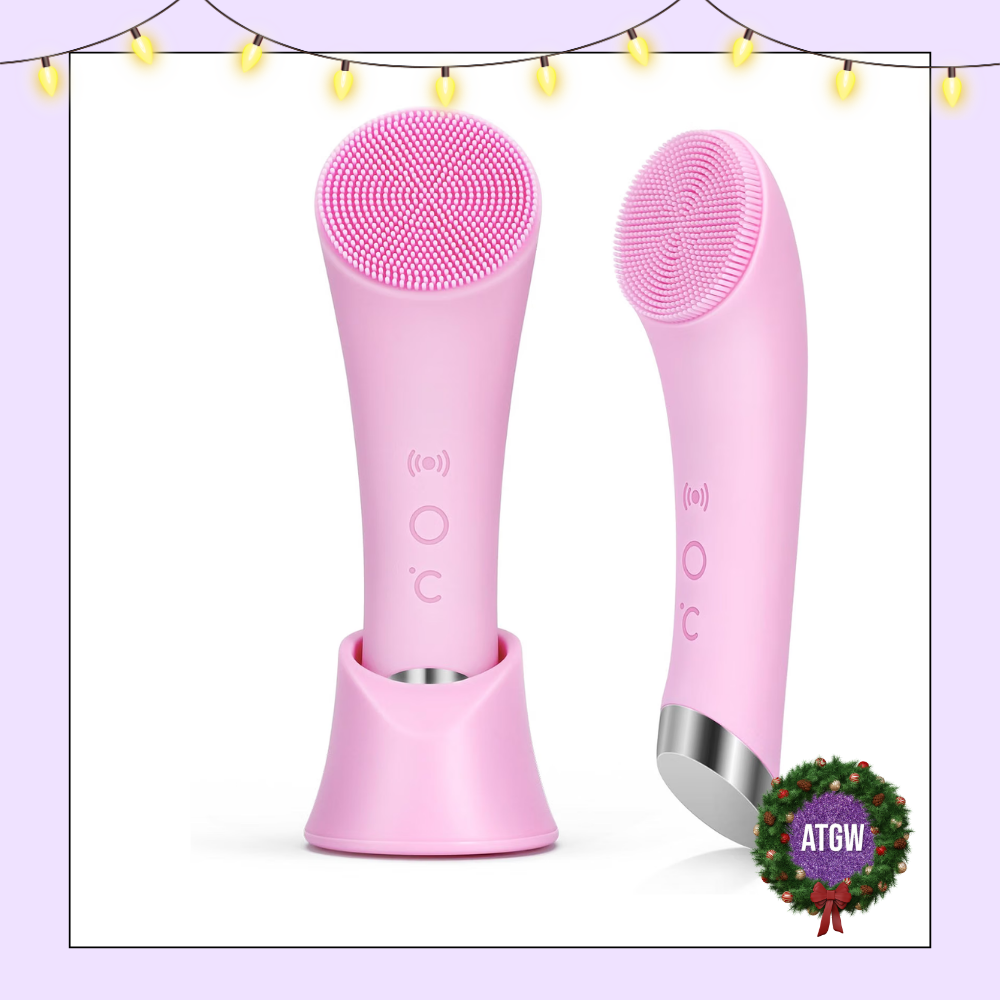 Soft pink handheld silicone facial cleansing brush sitting next to its matching upright countertop stand.