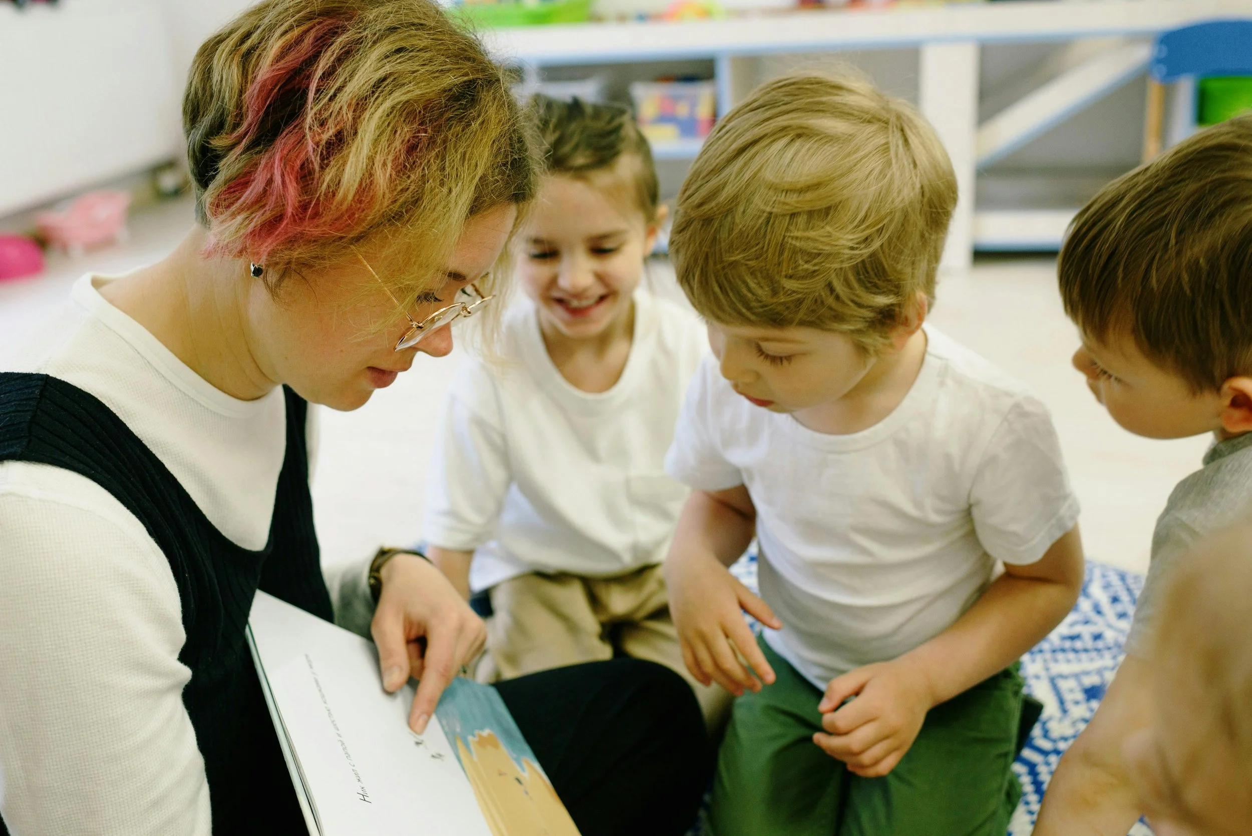teaching assistant reading a story to 3 children