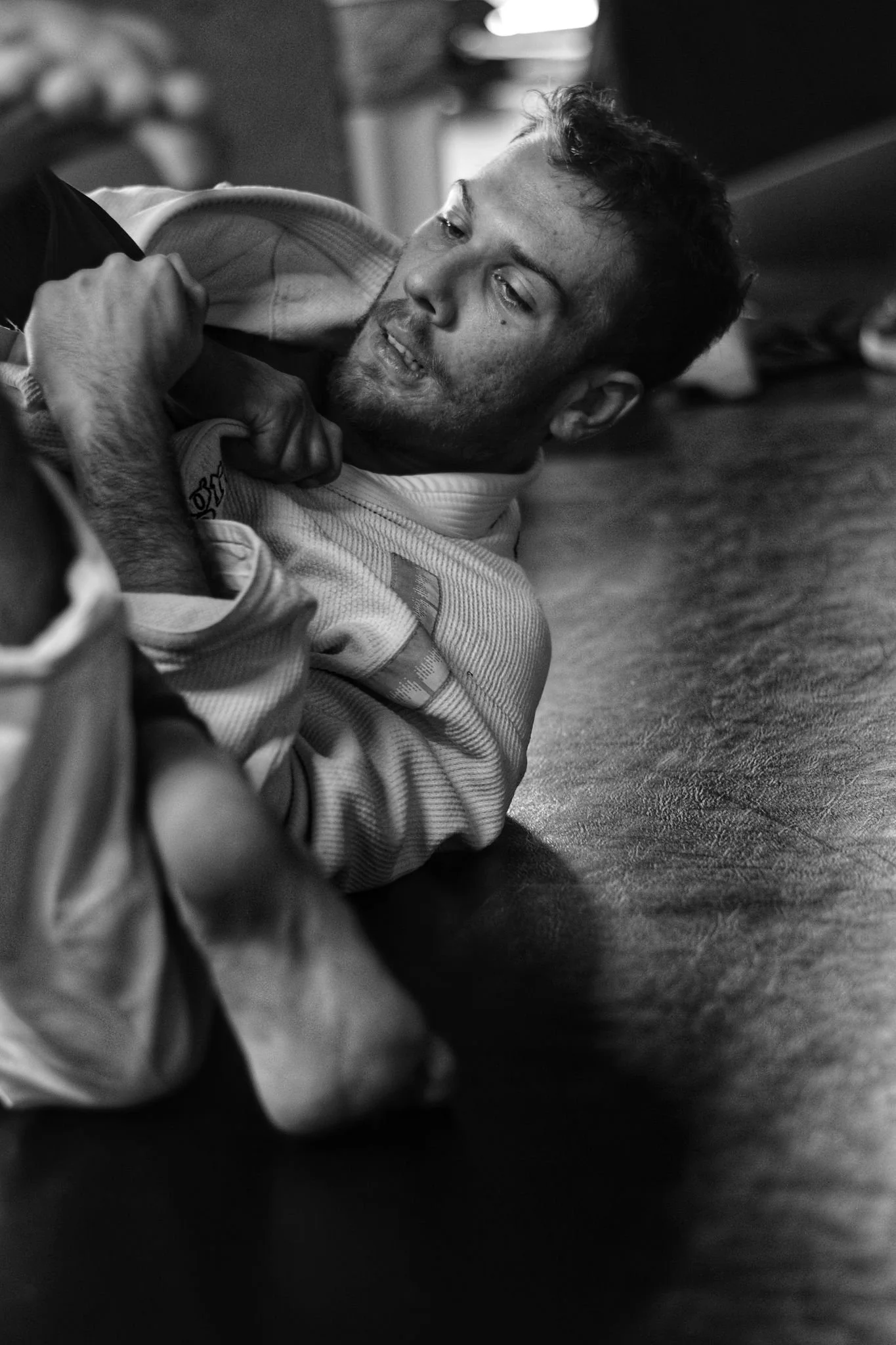 Un homme en kimono de jiu jitsu au sol lors d'une séance d'entraînement ou compétition, en train de se disputer ou être neutralisé sur le tapis.
